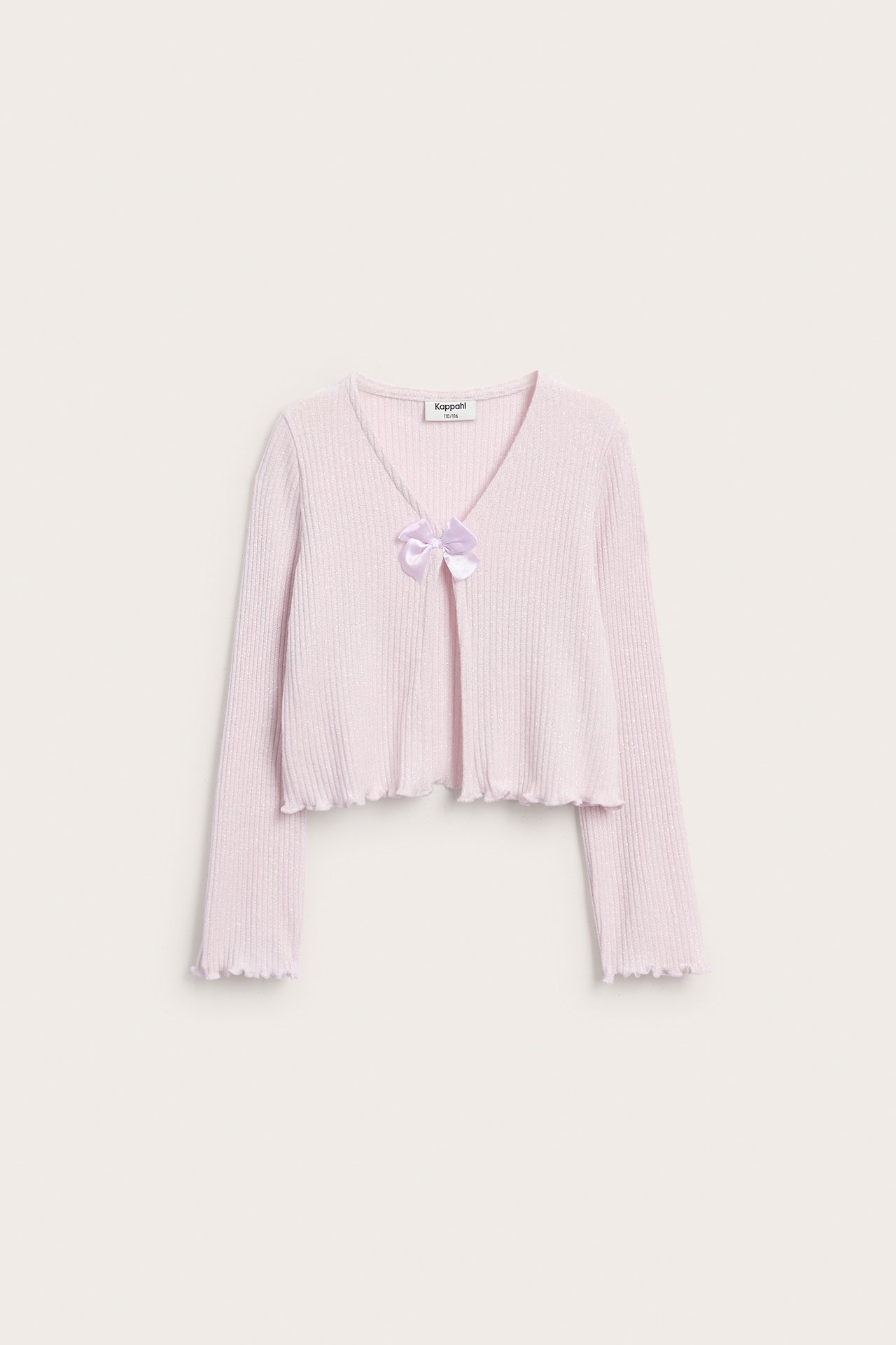 Edestä näkymä vaaleanpunaisesta lasten neuleesta, jossa on resori, V-pääntie, röyhelöt ja lila rusetti.
