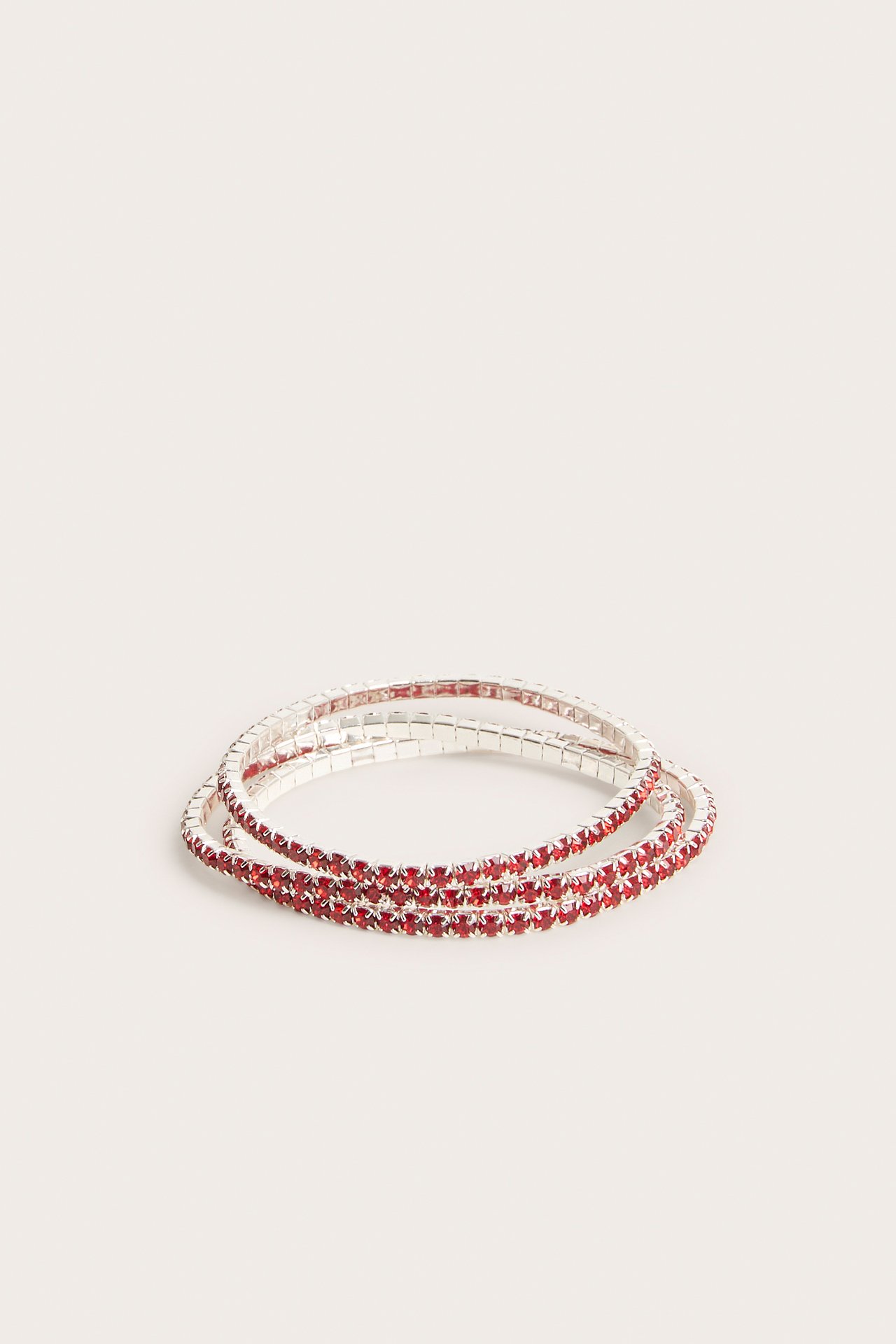 Framifrån, tre staplade silverfärgade stretcharmband med rader av röda strassstenar.