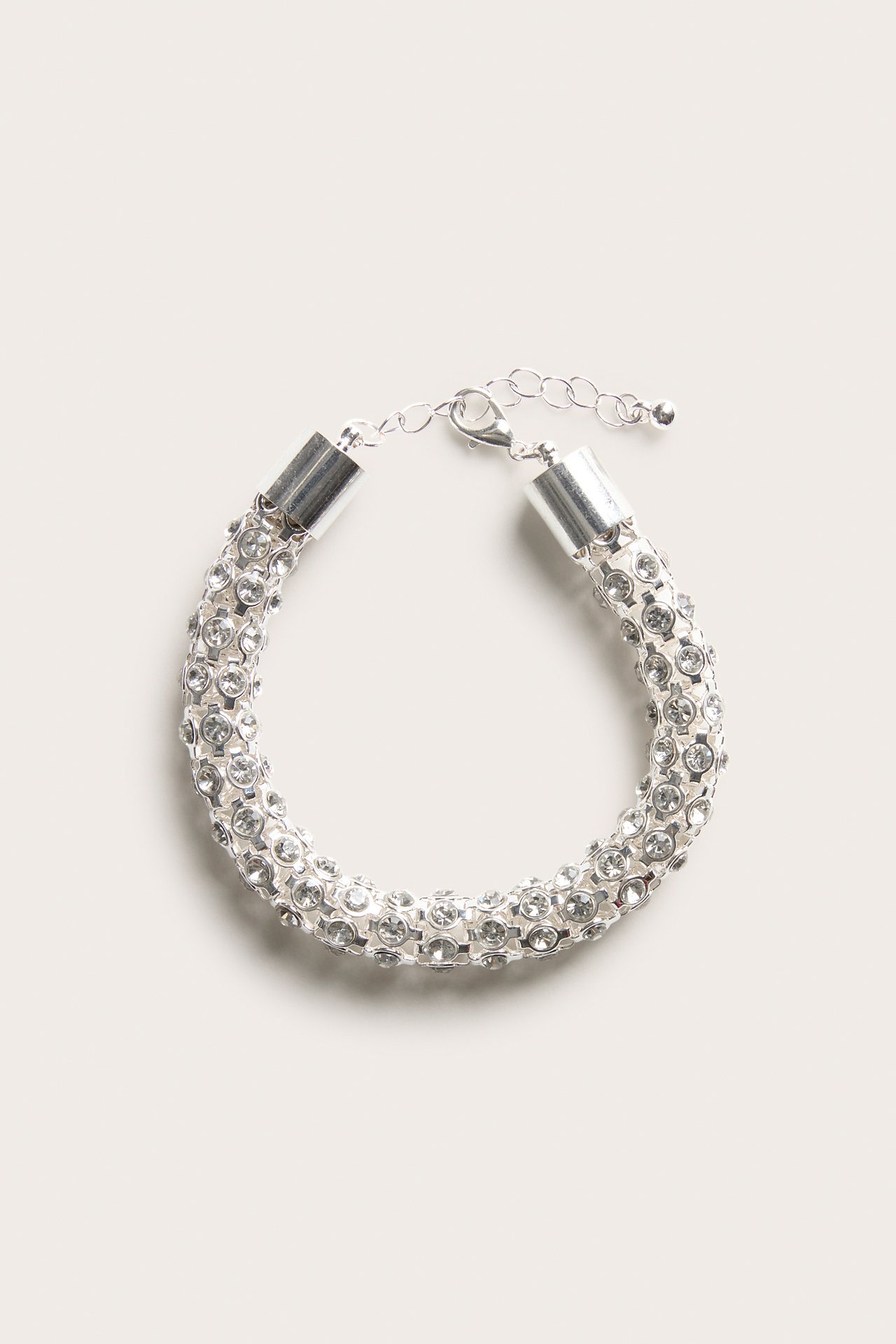 Ovanifrån vy av ett silverfärgat armband med klara kristaller och justerbart spänne.