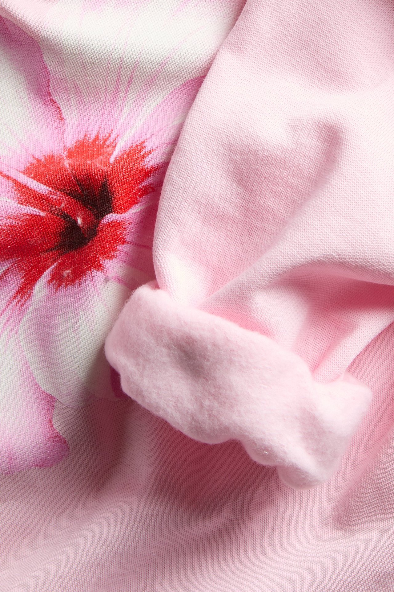 Zbliżenie na różową bluzę z kapturem z dużym kwiatowym nadrukiem i podwiniętym mankietem.