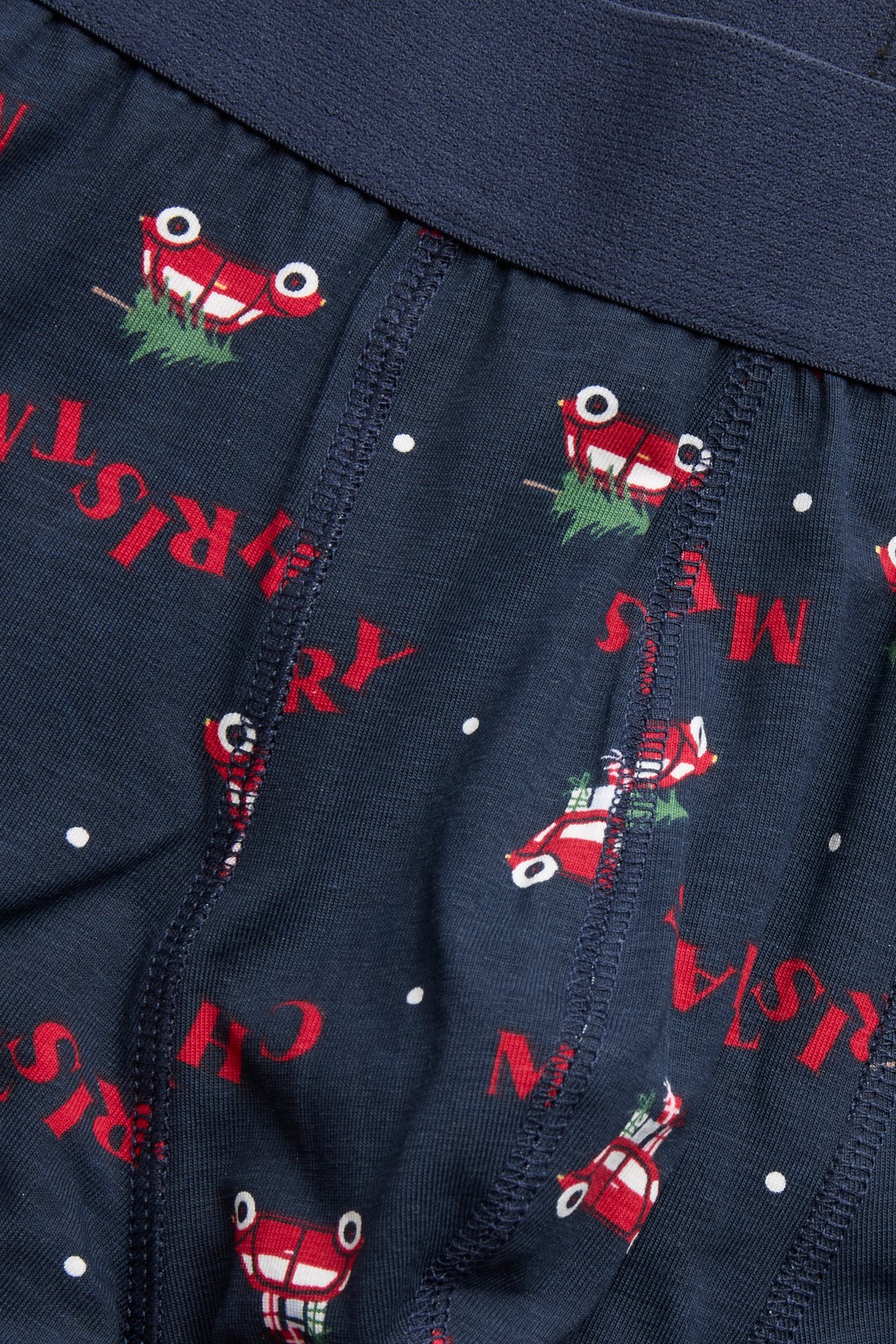 Nærbilde av mørkeblå boksershorts med rødt bil- og 'Merry Christmas'-teksttrykk.