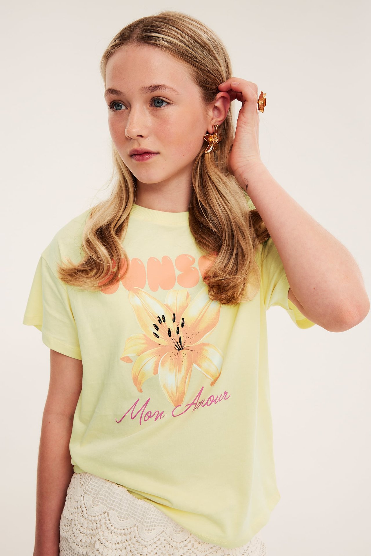Kvinna bär en ljusgul T-shirt med blomster- och textprint, framstående motiv.