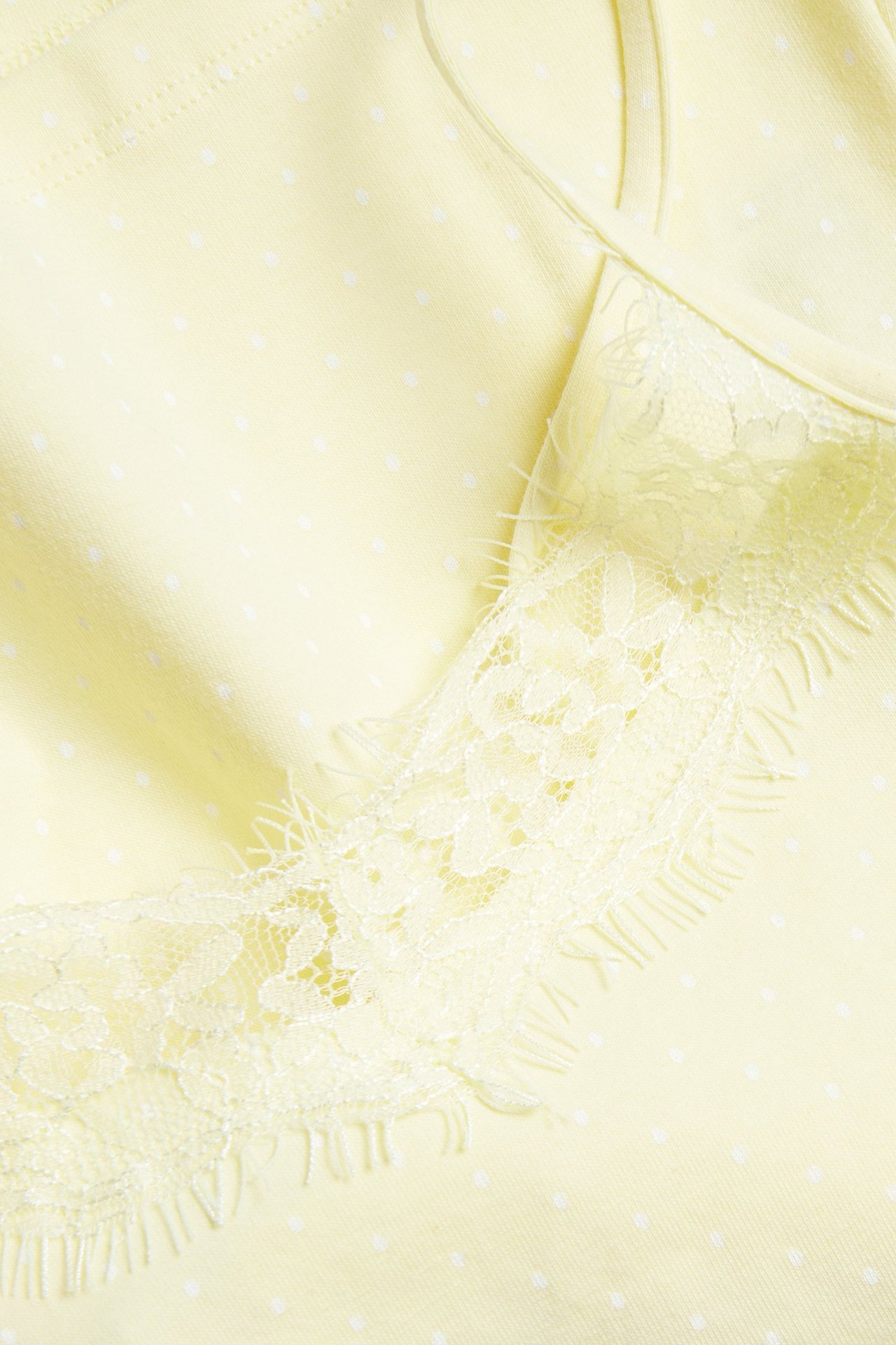 Zbliżenie na jasnożółtą bluzkę na ramiączkach z białymi kropkami i koronkową lamówką.