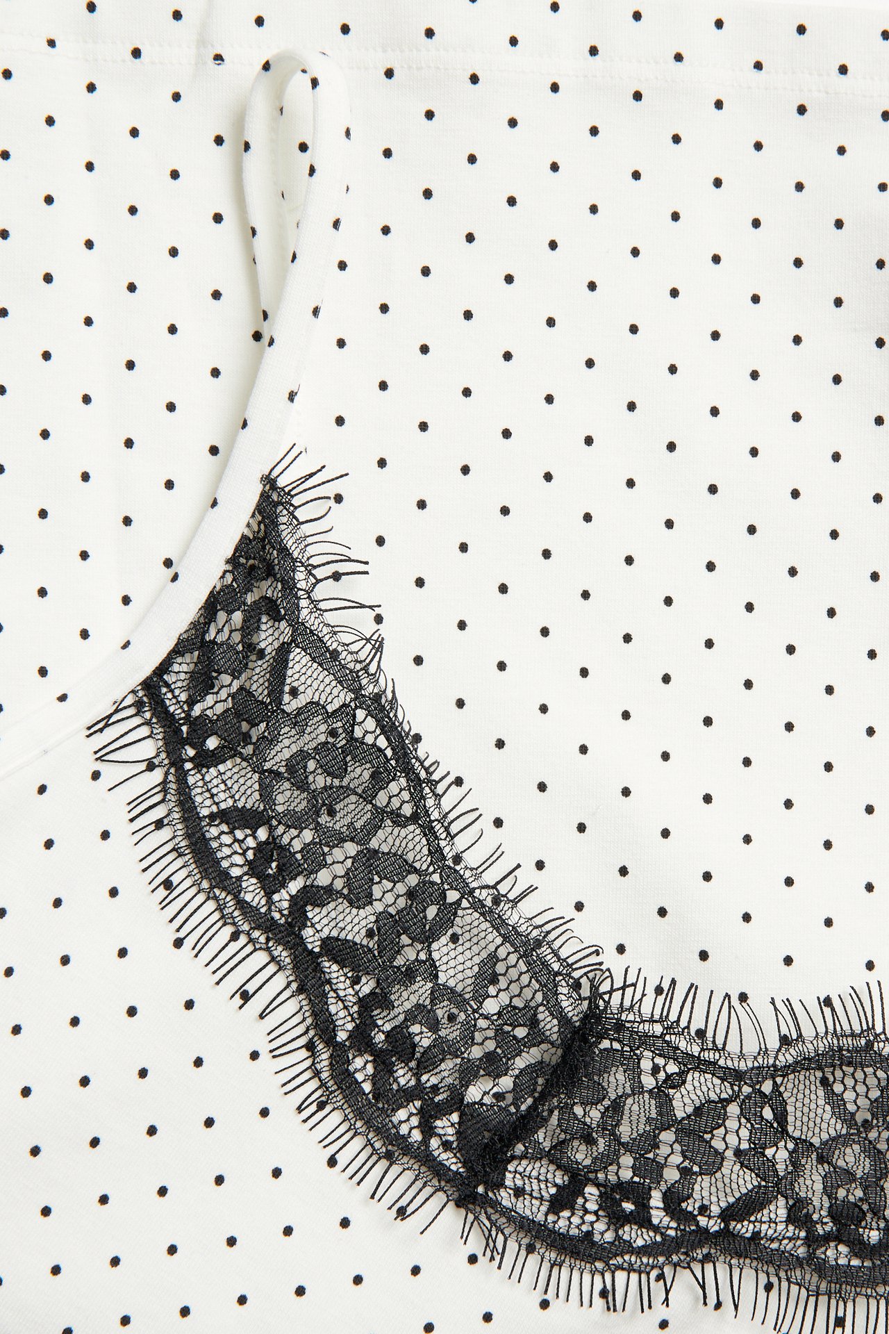 Zbliżenie na białą bluzkę z dżerseju w kropki z czarną koronkową lamówką przy dekolcie.