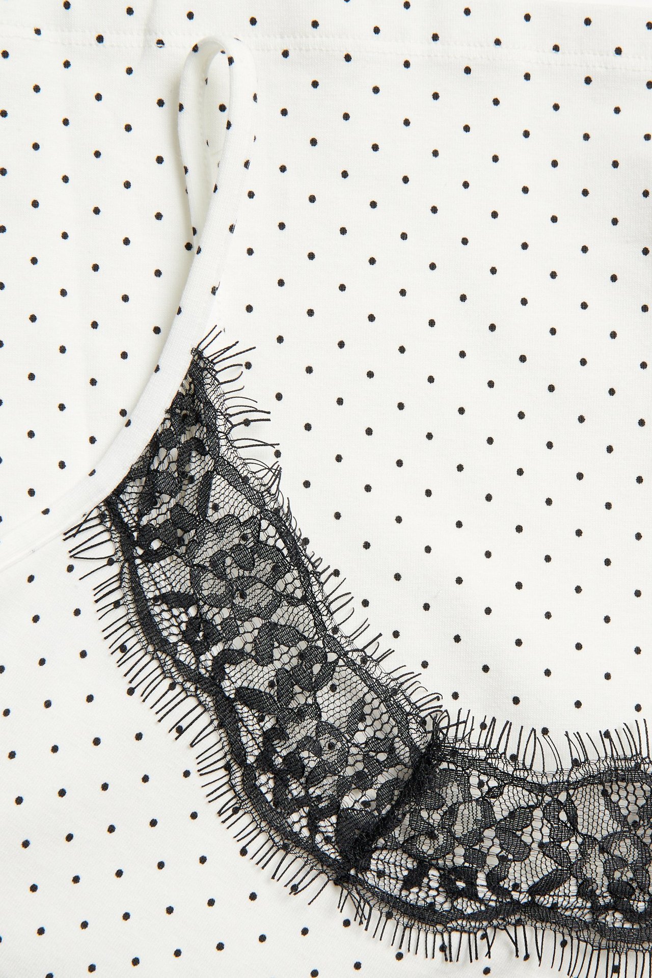 Zbliżenie na białą bluzkę z dżerseju w kropki z czarną koronkową lamówką przy dekolcie.