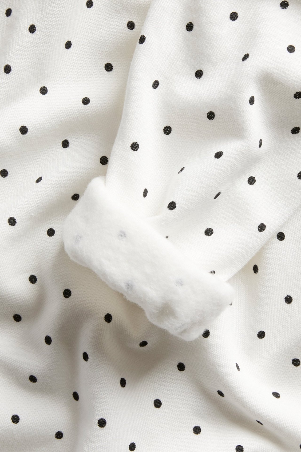 Zbliżenie rękawa białej bluzy z kapturem w czarne kropki, z miękkim, wywiniętym białym mankietem.