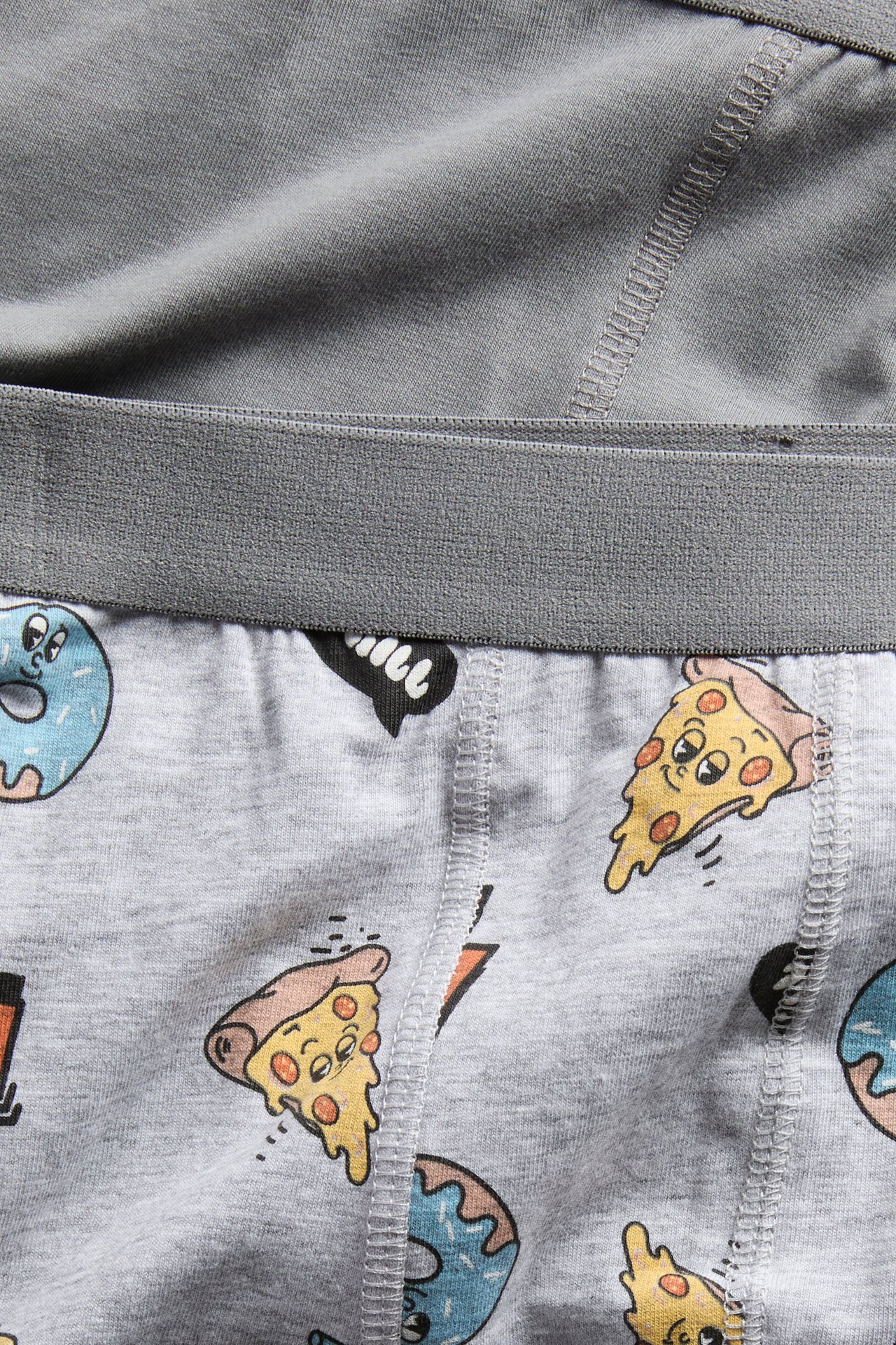 Närbild på gråa jerseykalsonger med färgglatt tecknat pizza- och munkmönster.