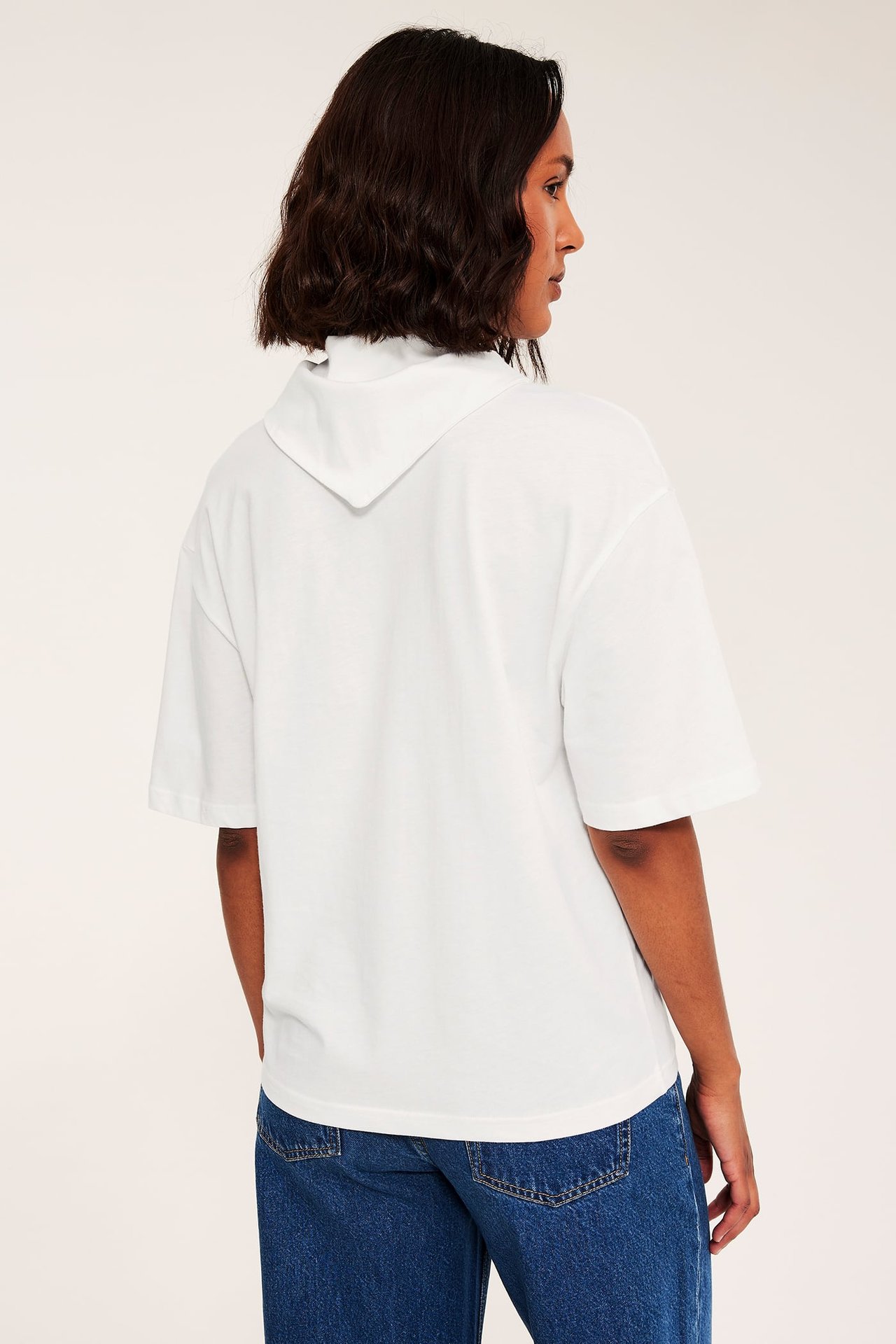 Ryggvy av kvinnlig modell i en oversized vit kortärmad pikétröja och blå jeans.