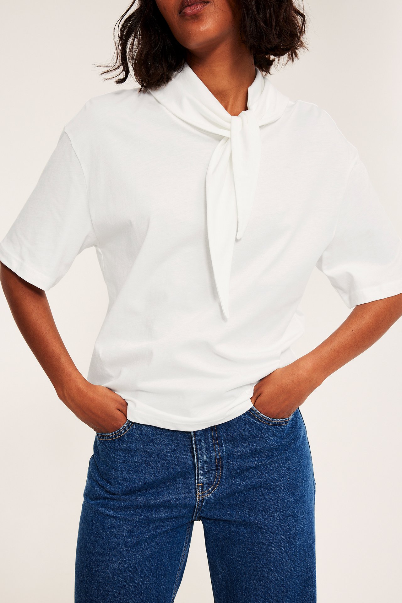 Framifrån kvinna i vit t-shirt med knyt och blå jeans.