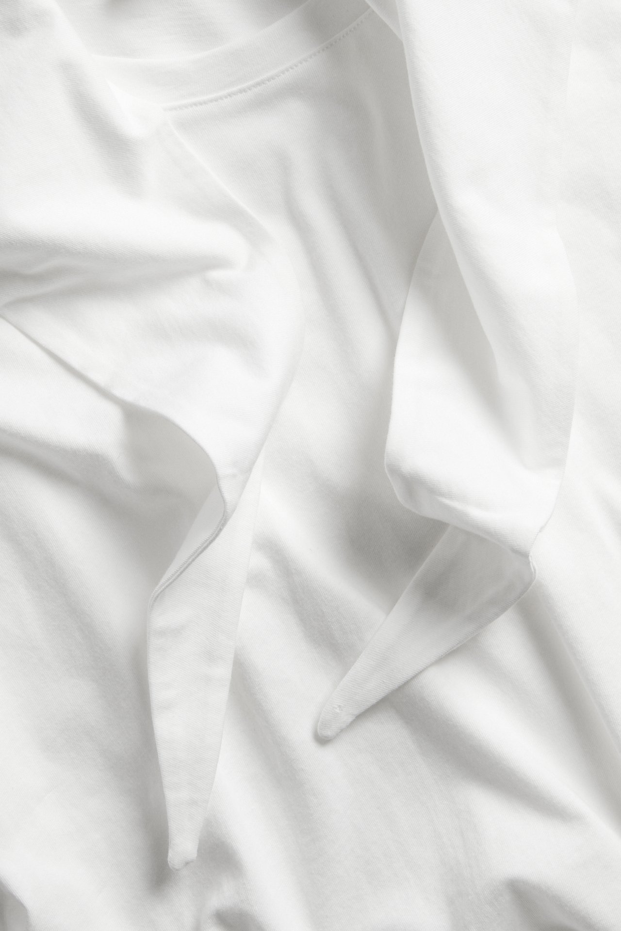 Närbild av en offwhite T-shirt i bomull med fäst, draperad sjaldetalj.