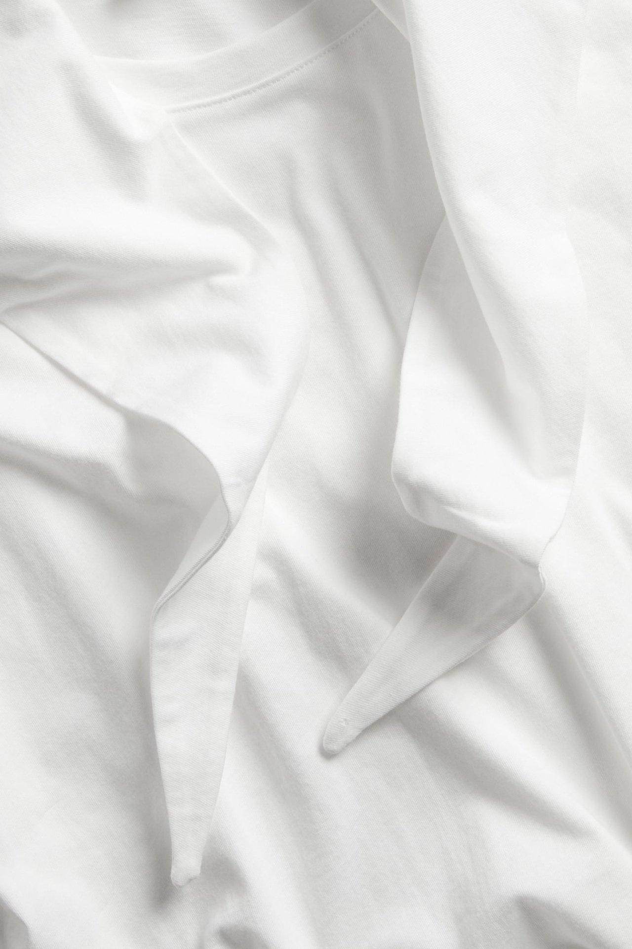 Zbliżenie na bawełniany T-shirt w kolorze ecru z doczepioną, udrapowaną ozdobą szala.