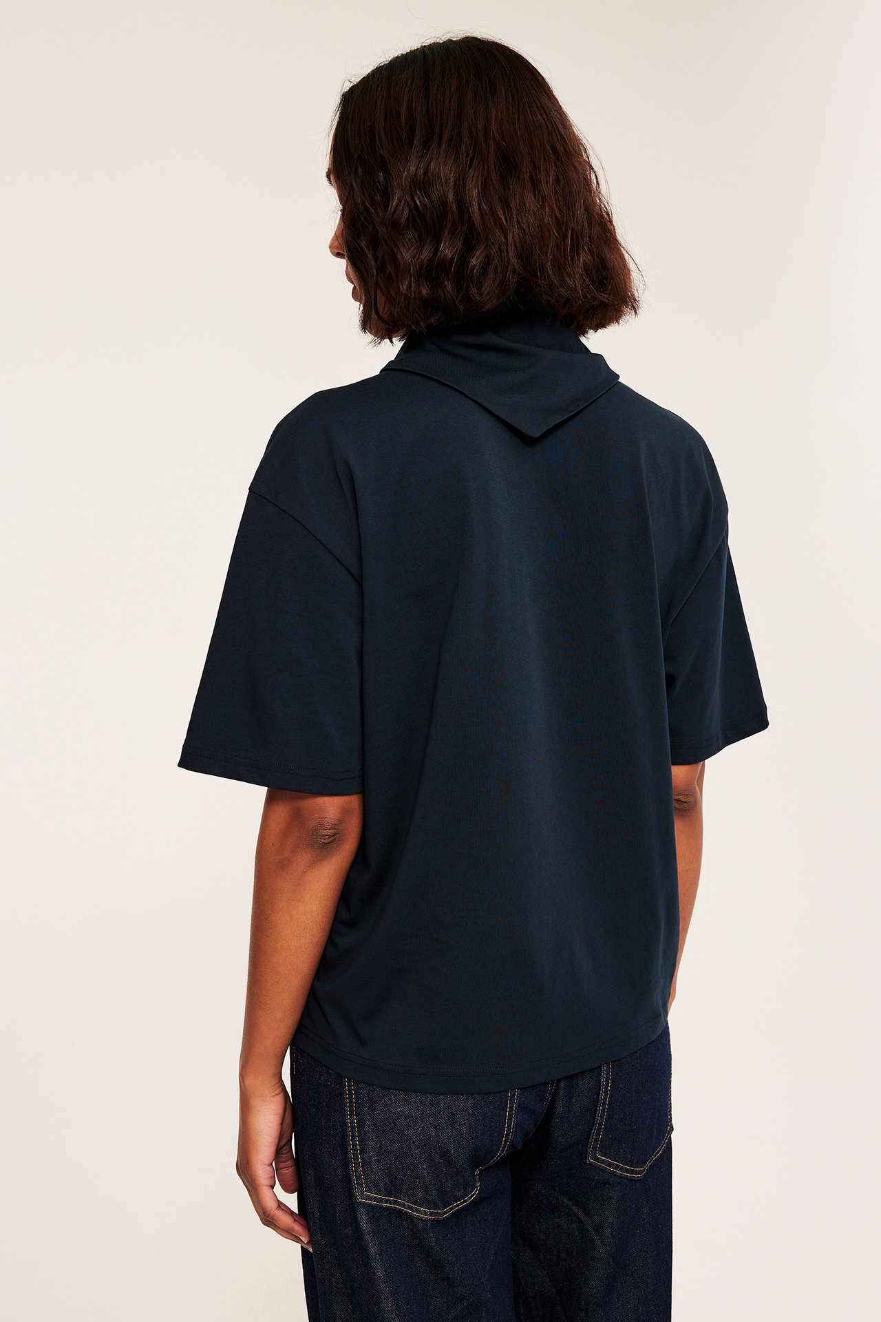Kvinna sedd bakifrån i en mörkblå överdimensionerad kortärmad topp med krage och mörkblå löst sittande jeans.
