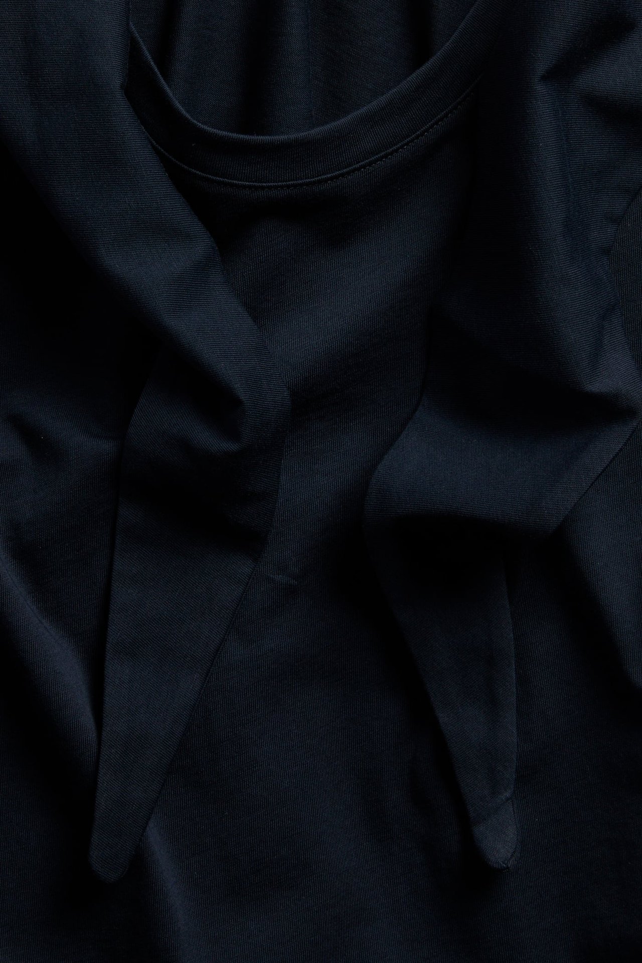 Zbliżenie ciemnoniebieskiego bawełnianego t-shirtu ze zintegrowanym detalem szalika przy dekolcie.