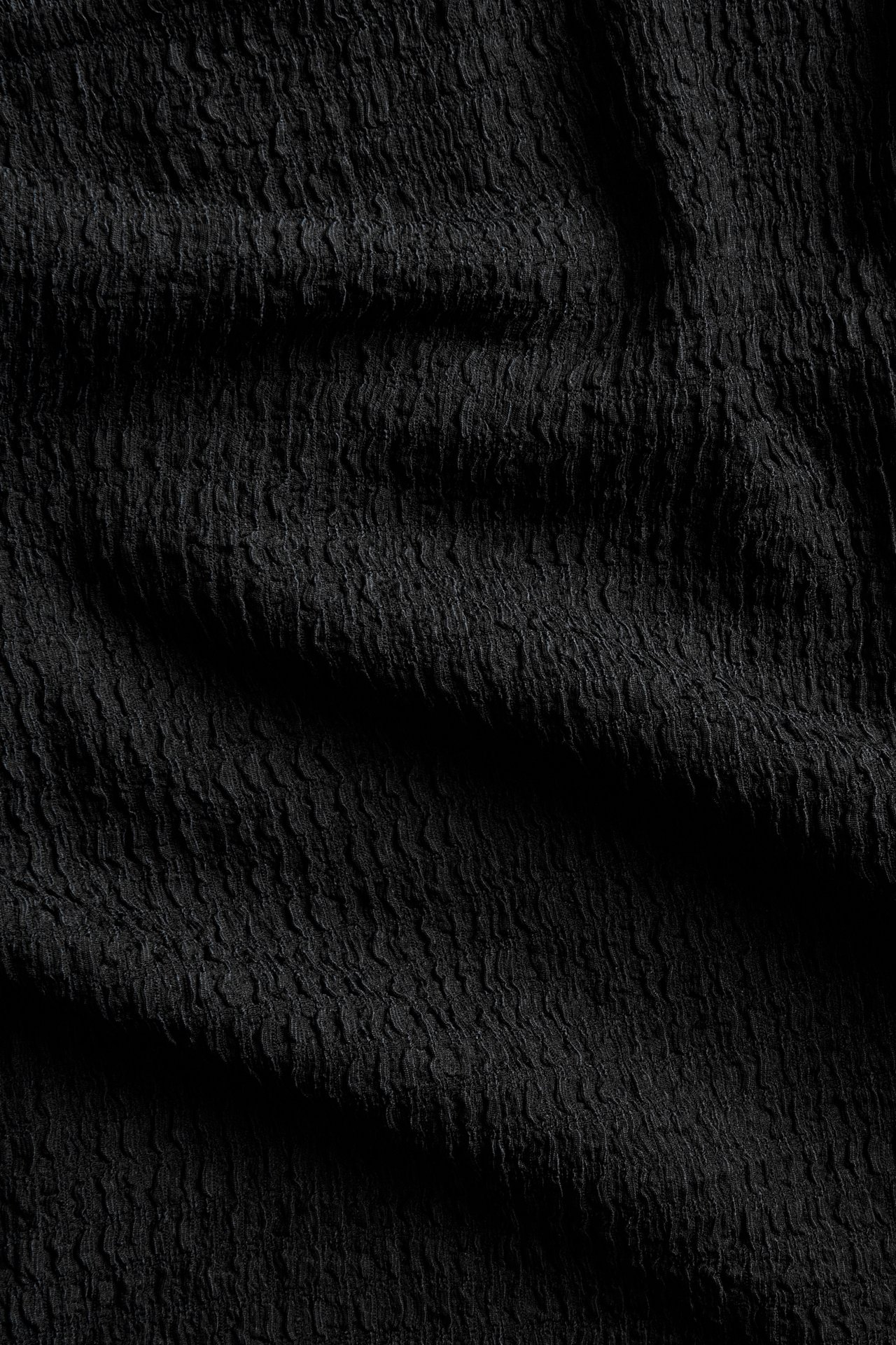 Närbild av svart strukturerat topptyg med vågigt, veckat mönster.