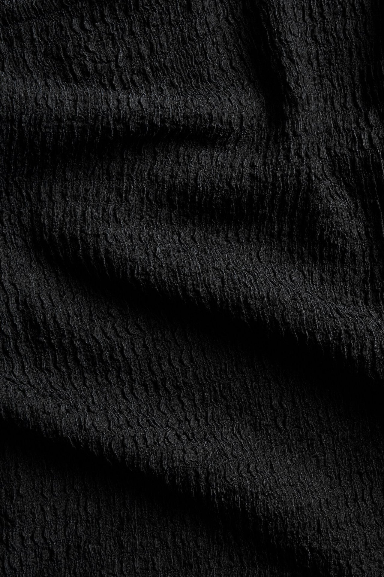 Zbliżenie czarnego, strukturalnego materiału bluzki z falistym, marszczonym wzorem.