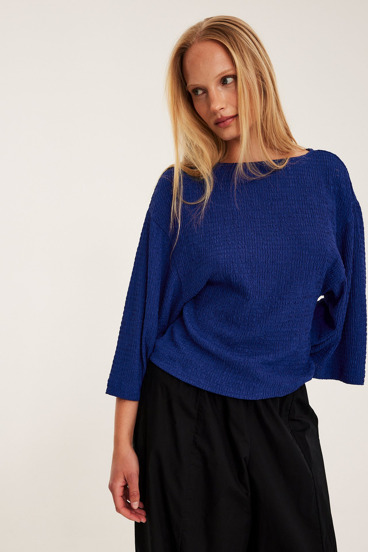 Edestä kuvattu nainen, yllään sininen kuvioitu toppi leveillä kimono-hihoilla ja mustat housut.