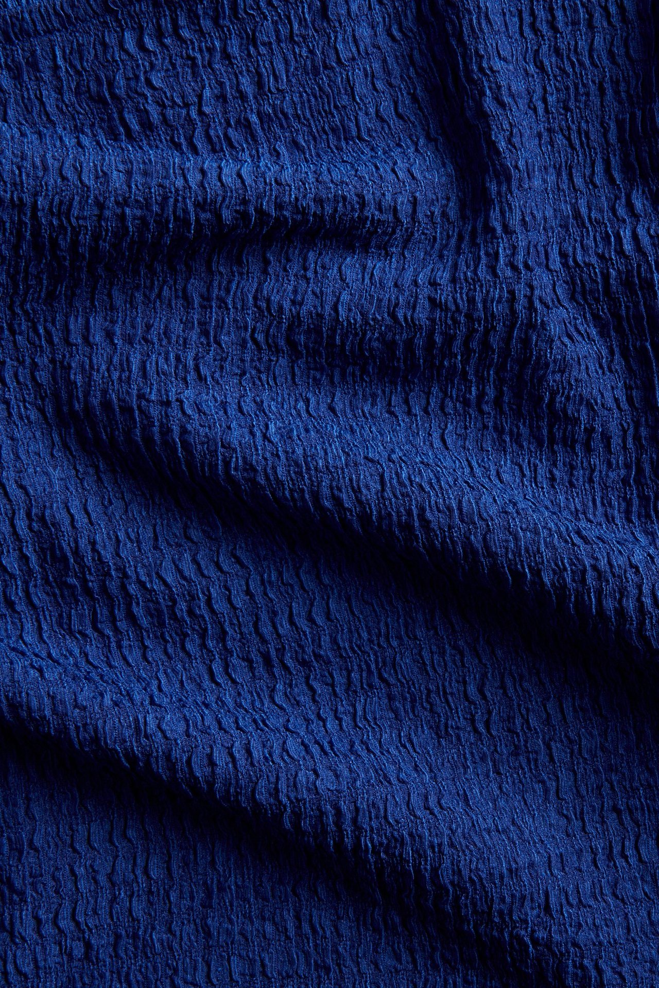 Zbliżenie na niebieską, fakturowaną tkaninę topu o pogniecionej teksturze.