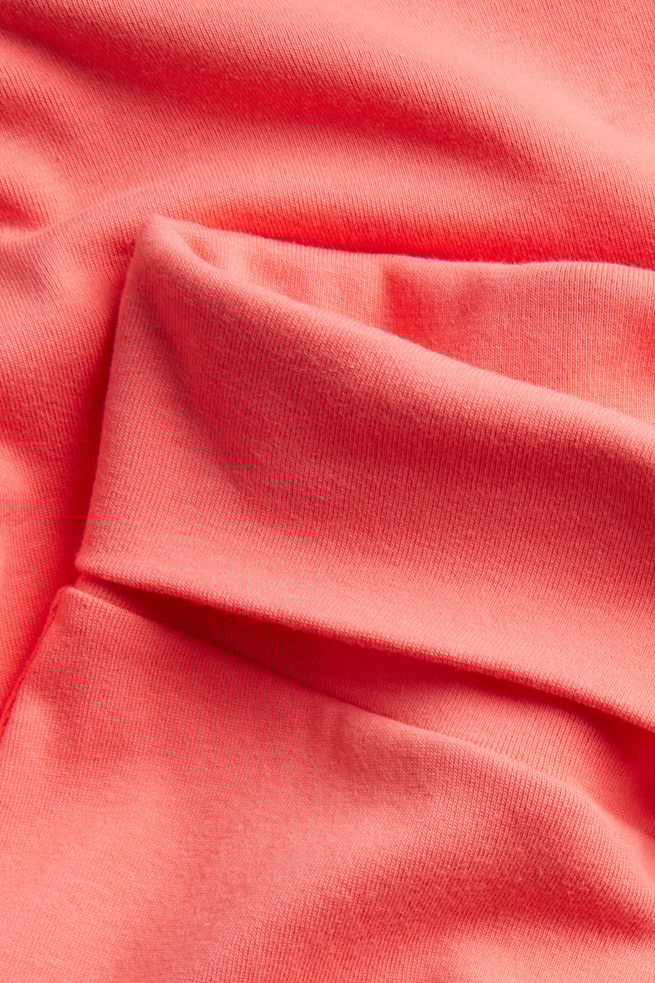 Zbliżenie na pomarańczowy, jednolity materiał spodni do jogi Vida z miękkimi zagięciami.