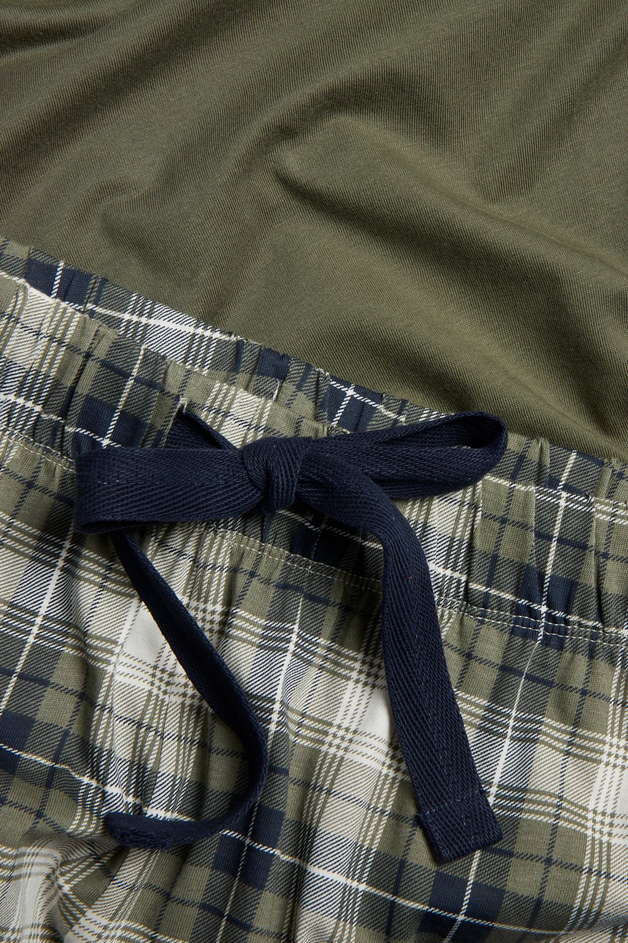 Lähikuva vihreä-siniruudullisista pyjamahousuista, sininen nyöri ja oliivinvihreä toppi.