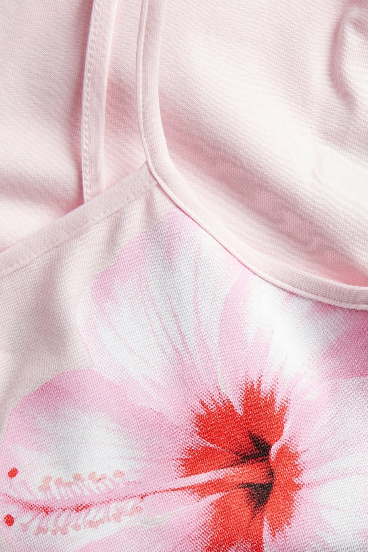 Zbliżenie jasnoróżowego topu dziecięcego z wąskimi ramiączkami i dużym różowo-czerwonym nadrukiem kwiatowym.