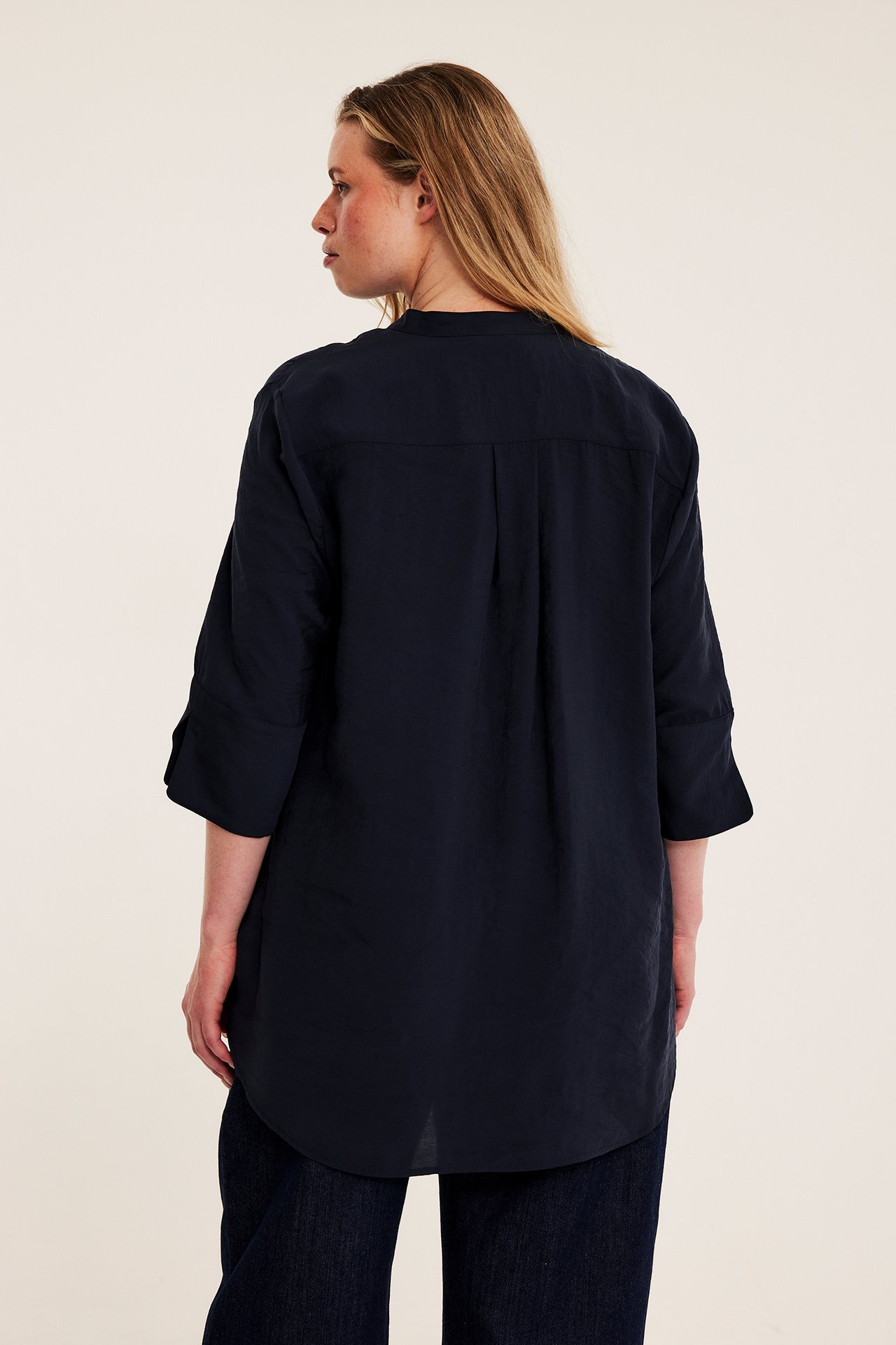 Bakifrån: kvinnlig modell i mörkblå oversized tunikaskjorta och mörkblå byxor.