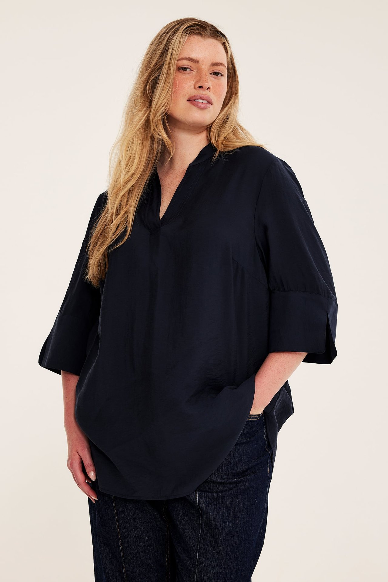 Framifrån: kvinna i mörkblå v-ringad blus med trekvartsärm och mörkblå jeans.