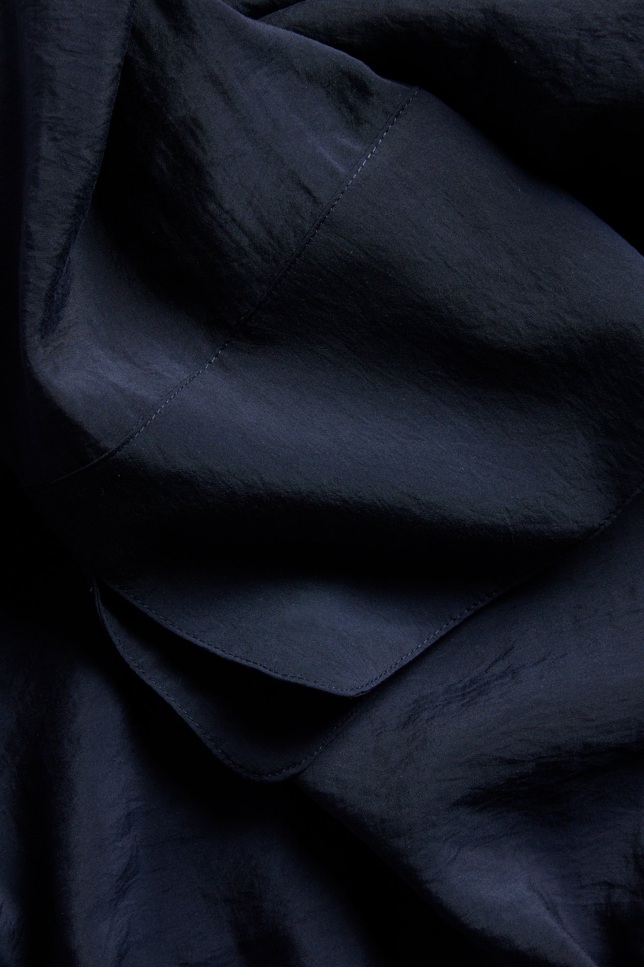 Närbild på mörkblått blustyg i modalblandning med synliga sömmar och draperade veck.