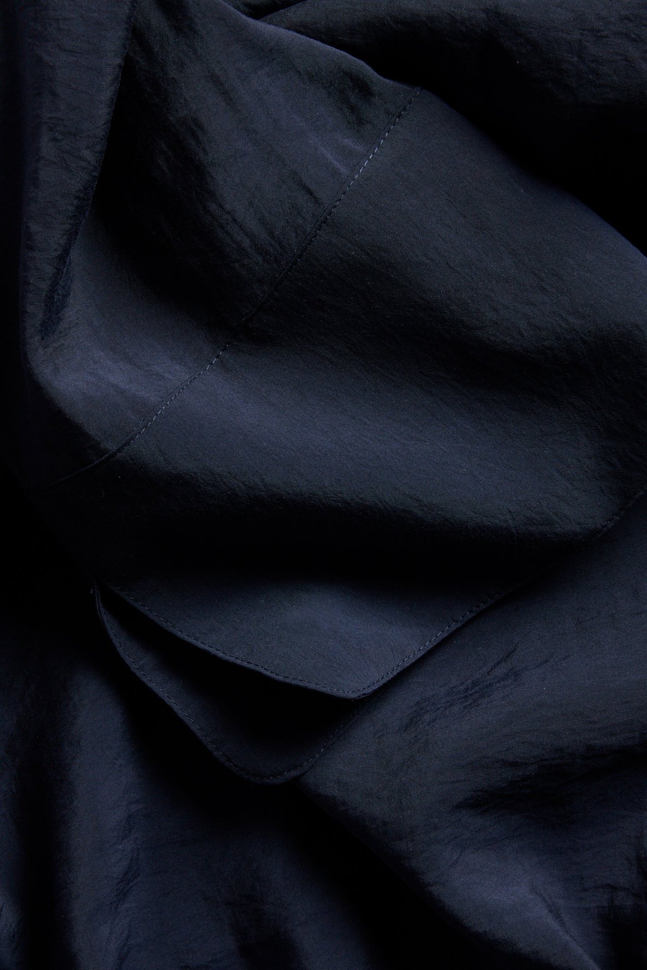 Närbild på mörkblått blustyg i modalblandning med synliga sömmar och draperade veck.