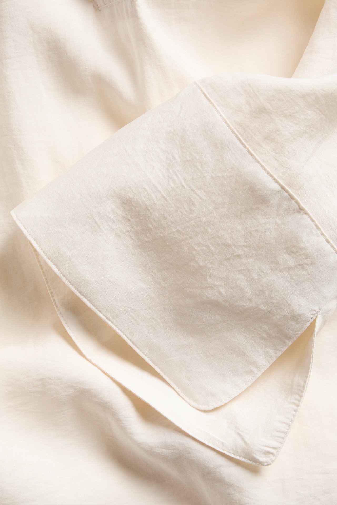 Närbild av en offwhite blusmanschett i modalmix, visar sidenliknande tyg och sömmar.