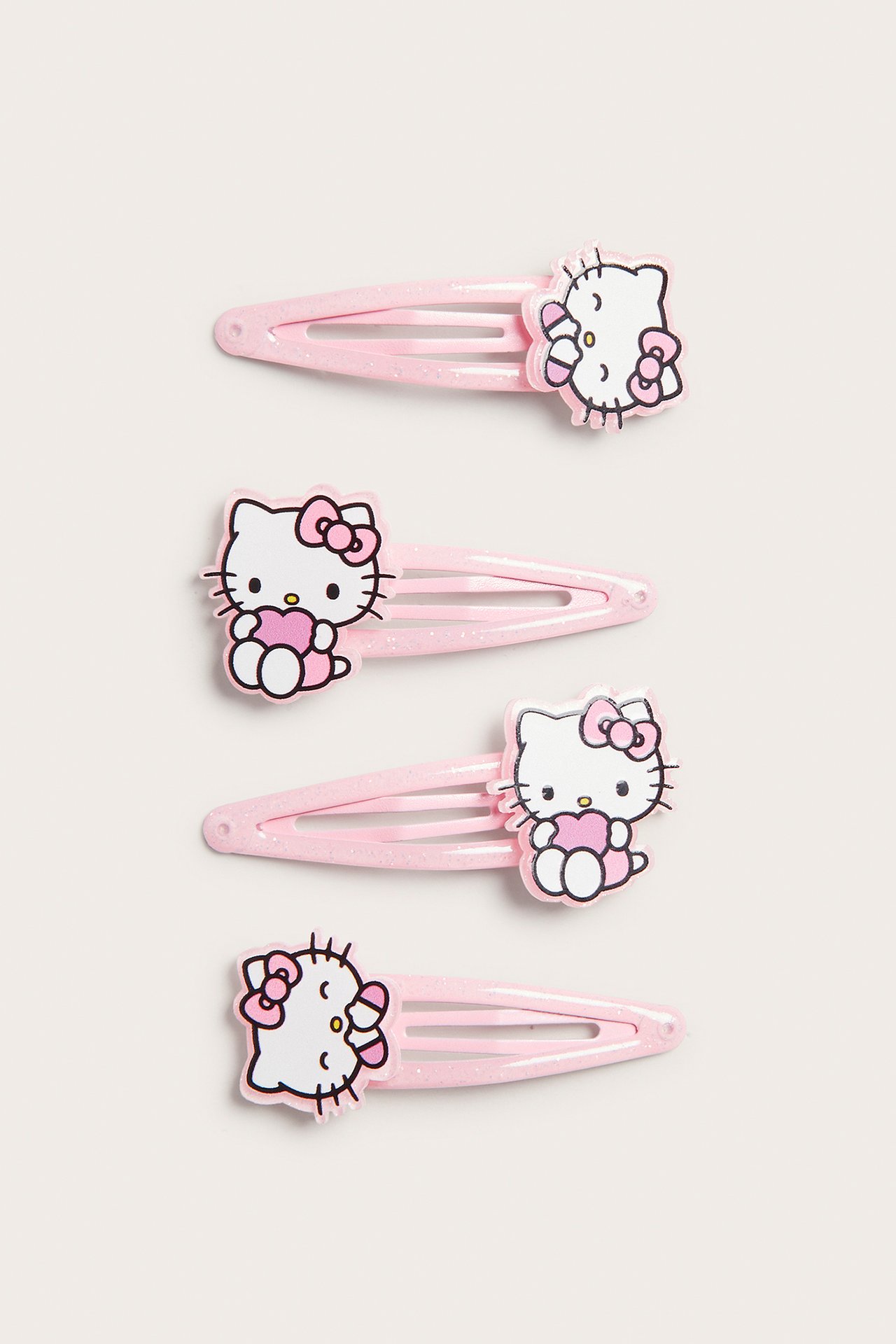 Widok z przodu na cztery różowe brokatowe spinki Hello Kitty z różowymi kokardkami.