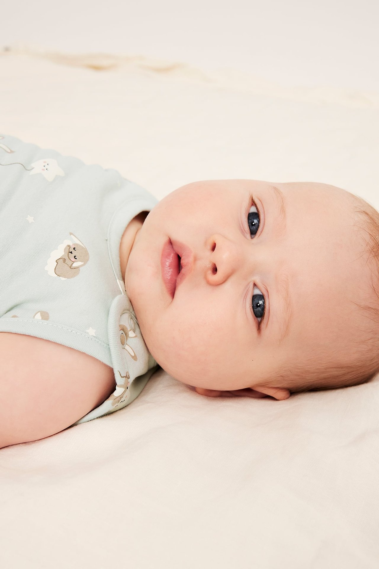 Nærbilde av baby i lyseblå kortermet body med dyre- og stjernemønster.