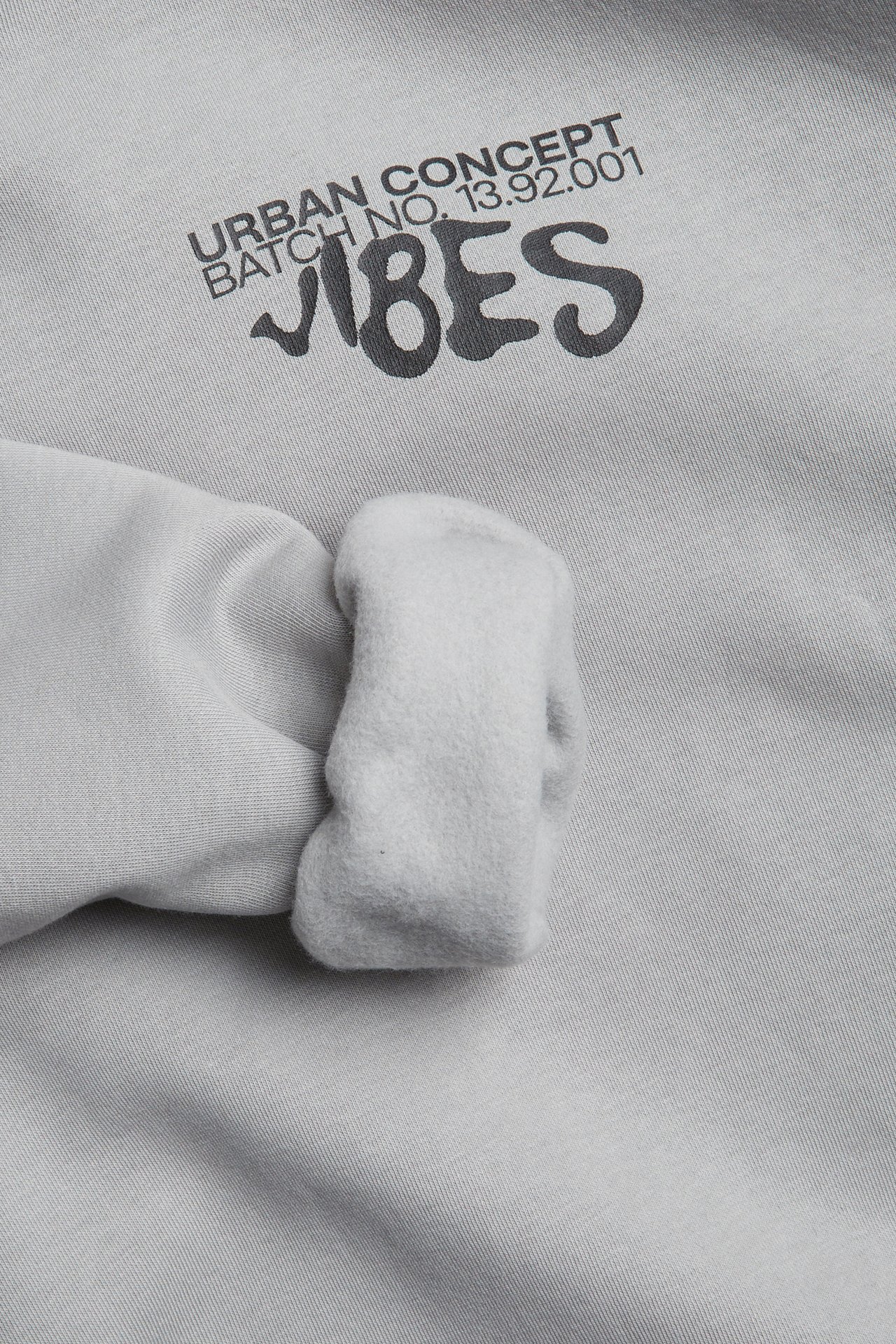 Närbild av en ljusgrå sweatshirt med svart 'URBAN CONCEPT VIBES'-tryck och synlig mudd.