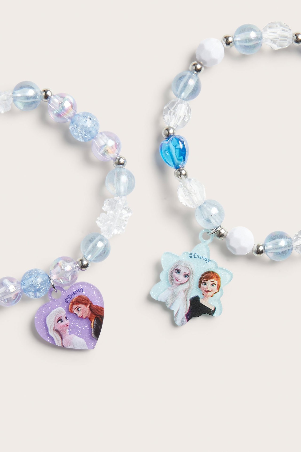 Dwie bransoletki Disney Frozen z niebieskimi, białymi koralikami i zawieszkami Elsy, Anny, zbliżenie.