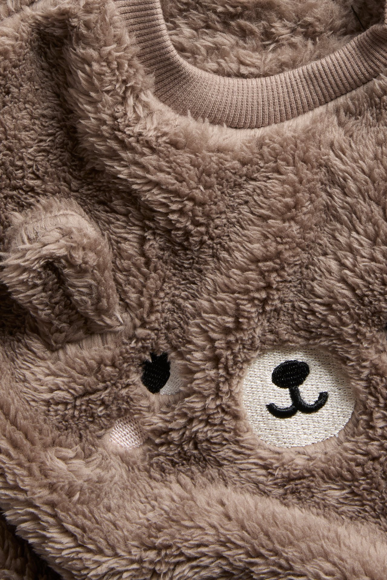 Zbliżenie na brązowy puszysty sweter niemowlęcy z prążkowanym kołnierzem i haftowanym pyskiem misia.