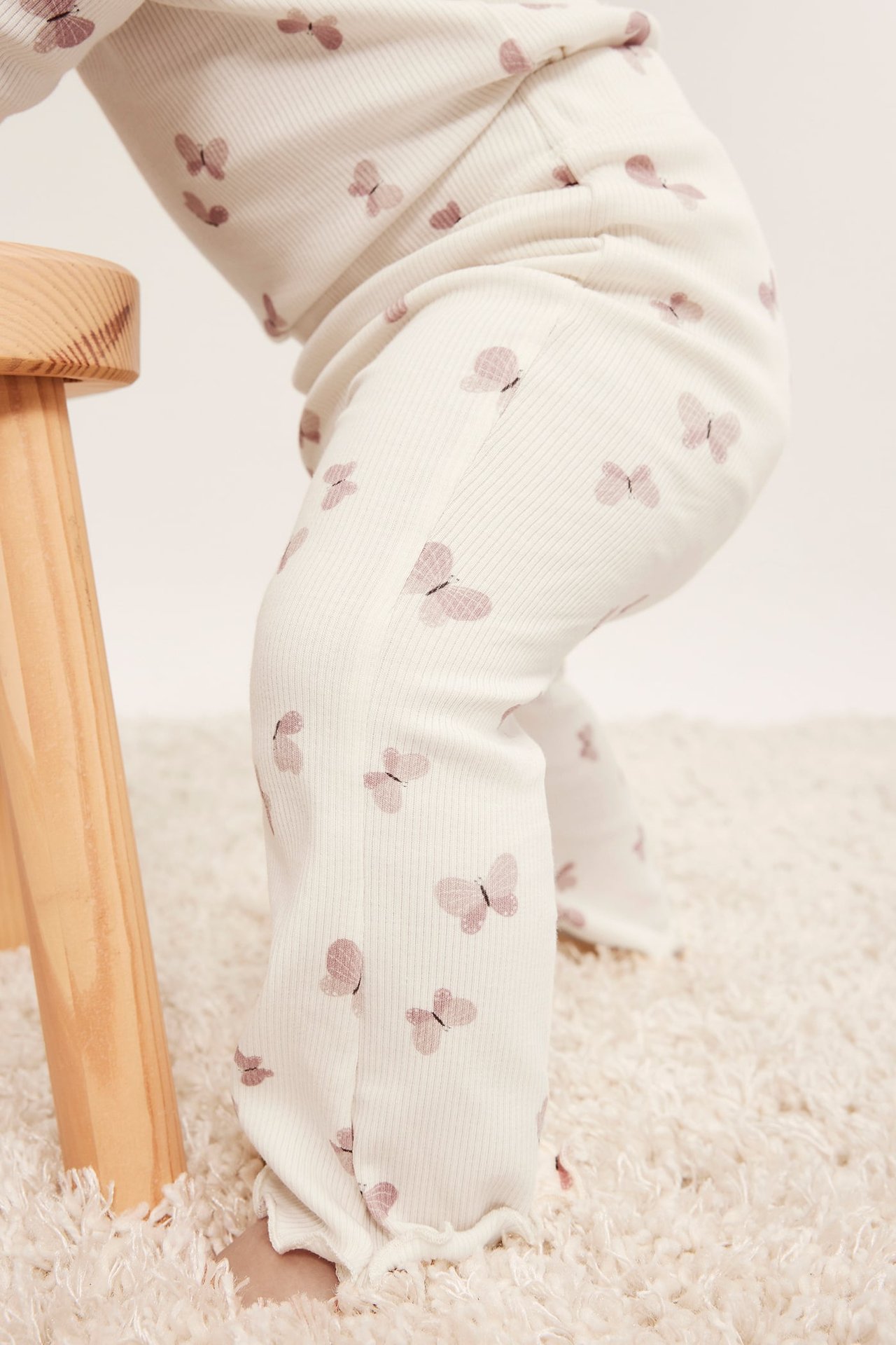 Lähikuva vauvasta kermanvärisessä, ribatussa pyjamasetissä vaaleanpunaisella perhospainatuksella.
