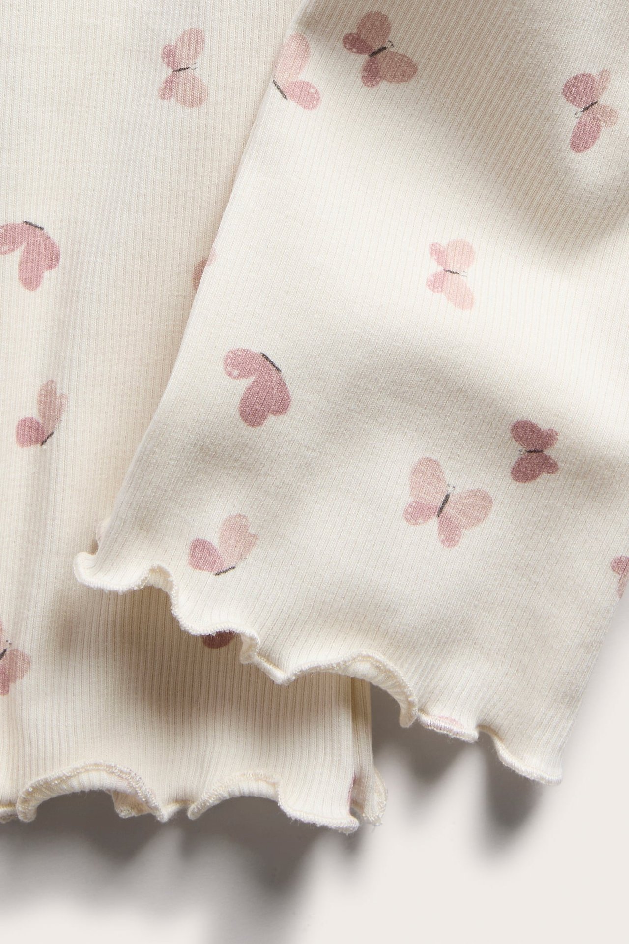 Närbild av gräddvita ribbade baby leggings med rosa fjärilsmönster och vågiga benslut.