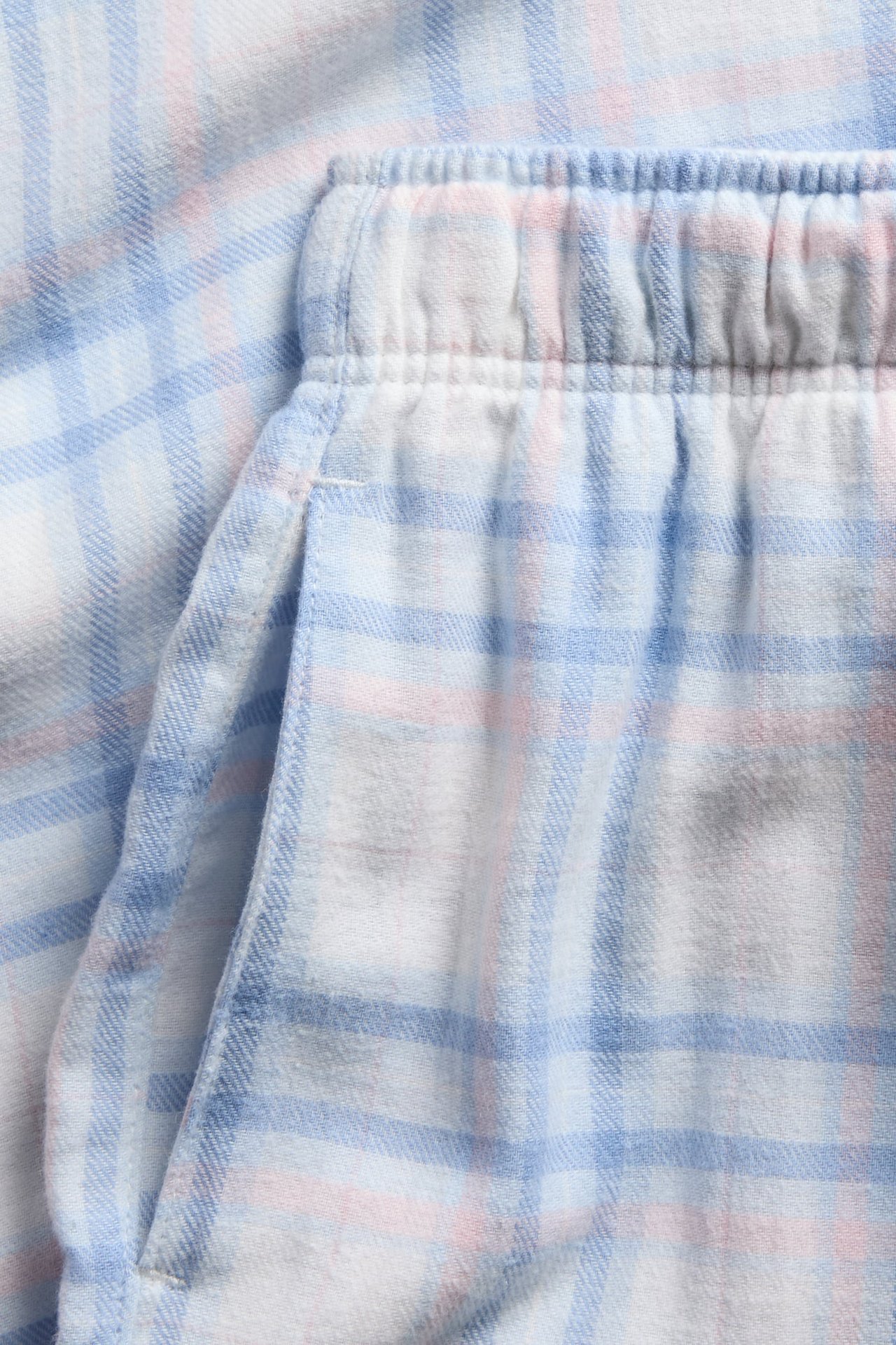 Nærbilde av blå og rosa rutete pyjamasbukser med elastisk linning og sidelomme.