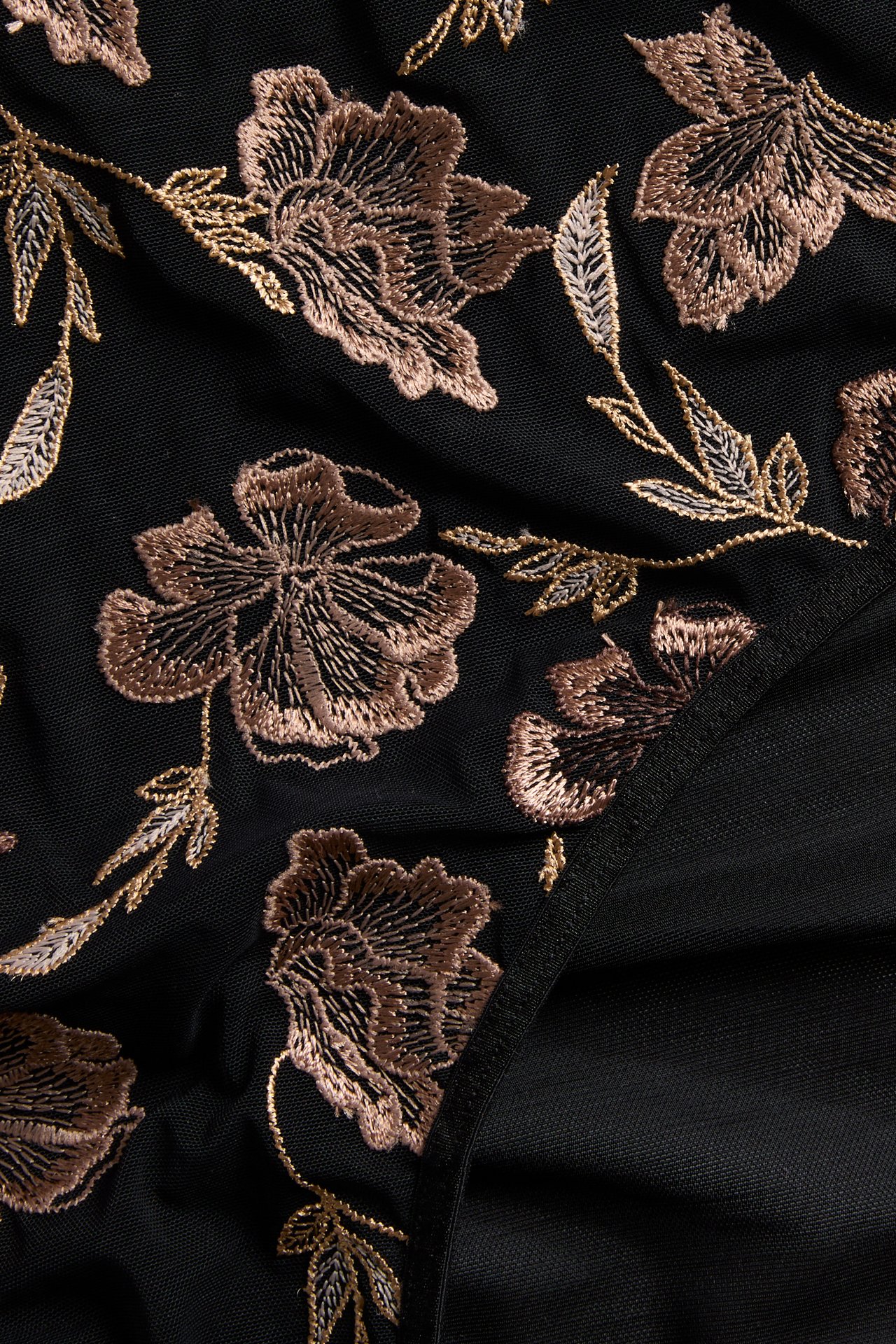 Nærbilde av svart stoff med gull- og brunblomstret broderi.