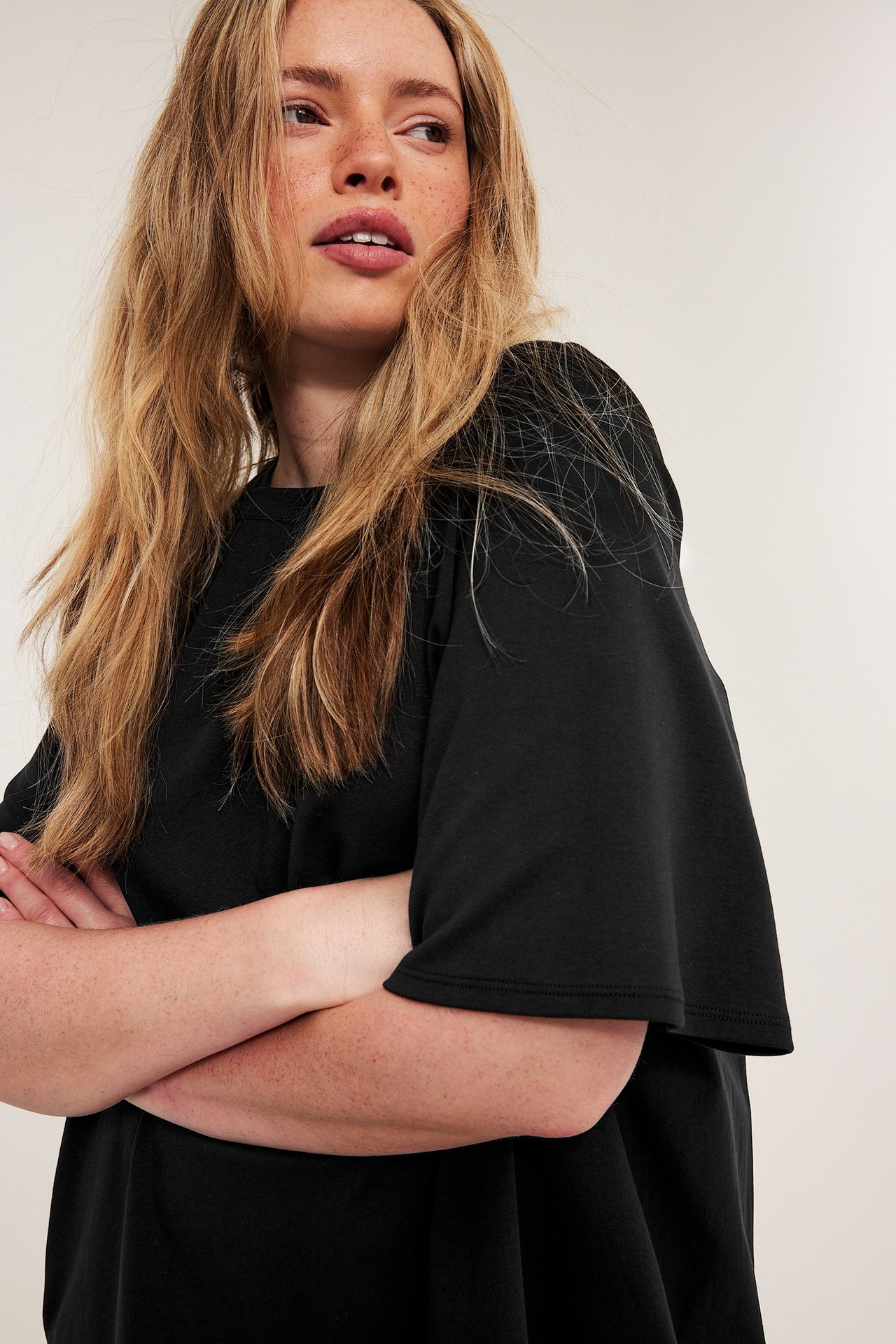 Nærbilde av en kvinne i en svart, løstsittende, kortermet jerseyt-skjortekjole med kryssede armer.
