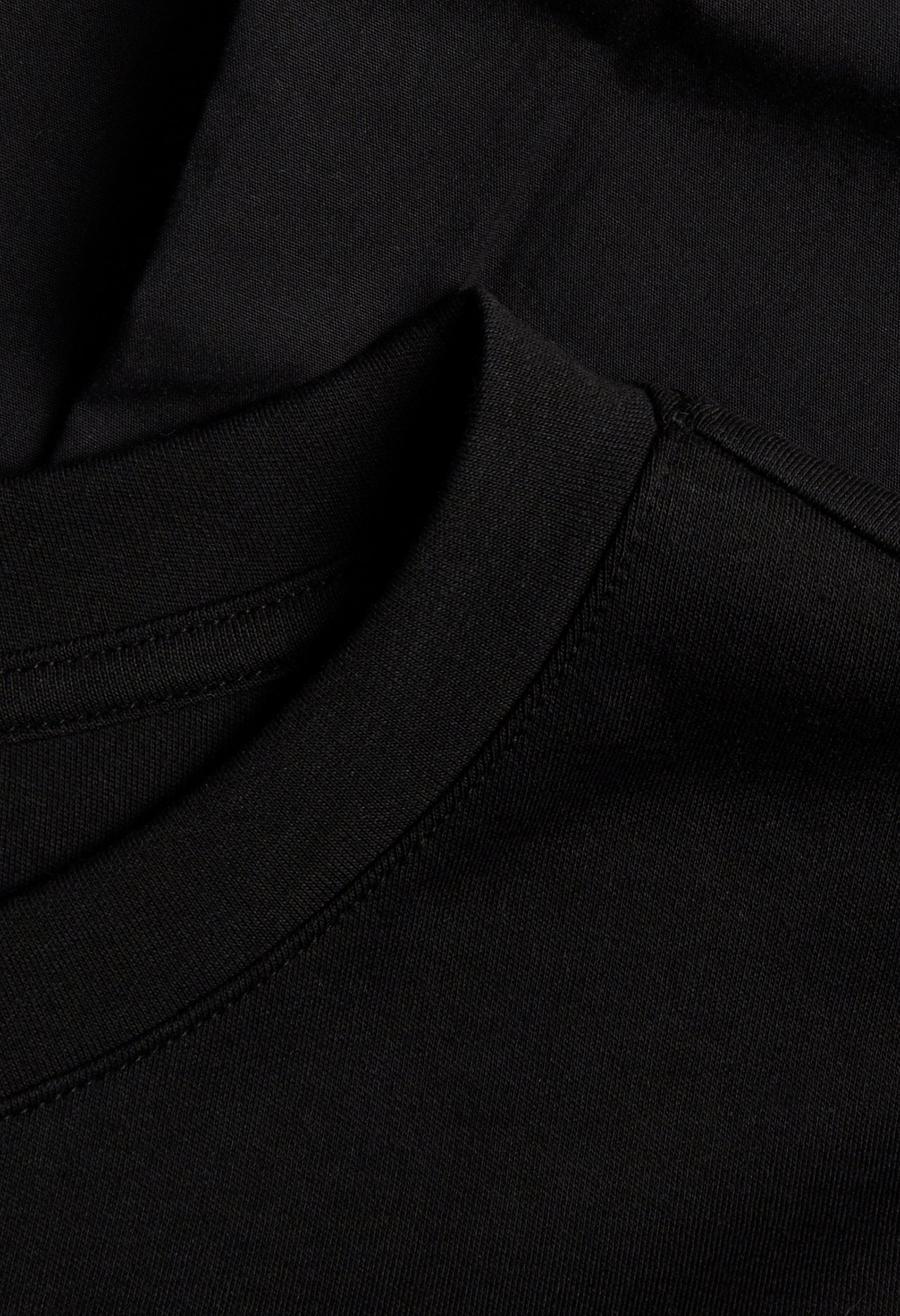 Nærbilde av en svart kort bomullsjersey T-skjortekjole, som viser den ribbestrikkede rundhalsen.