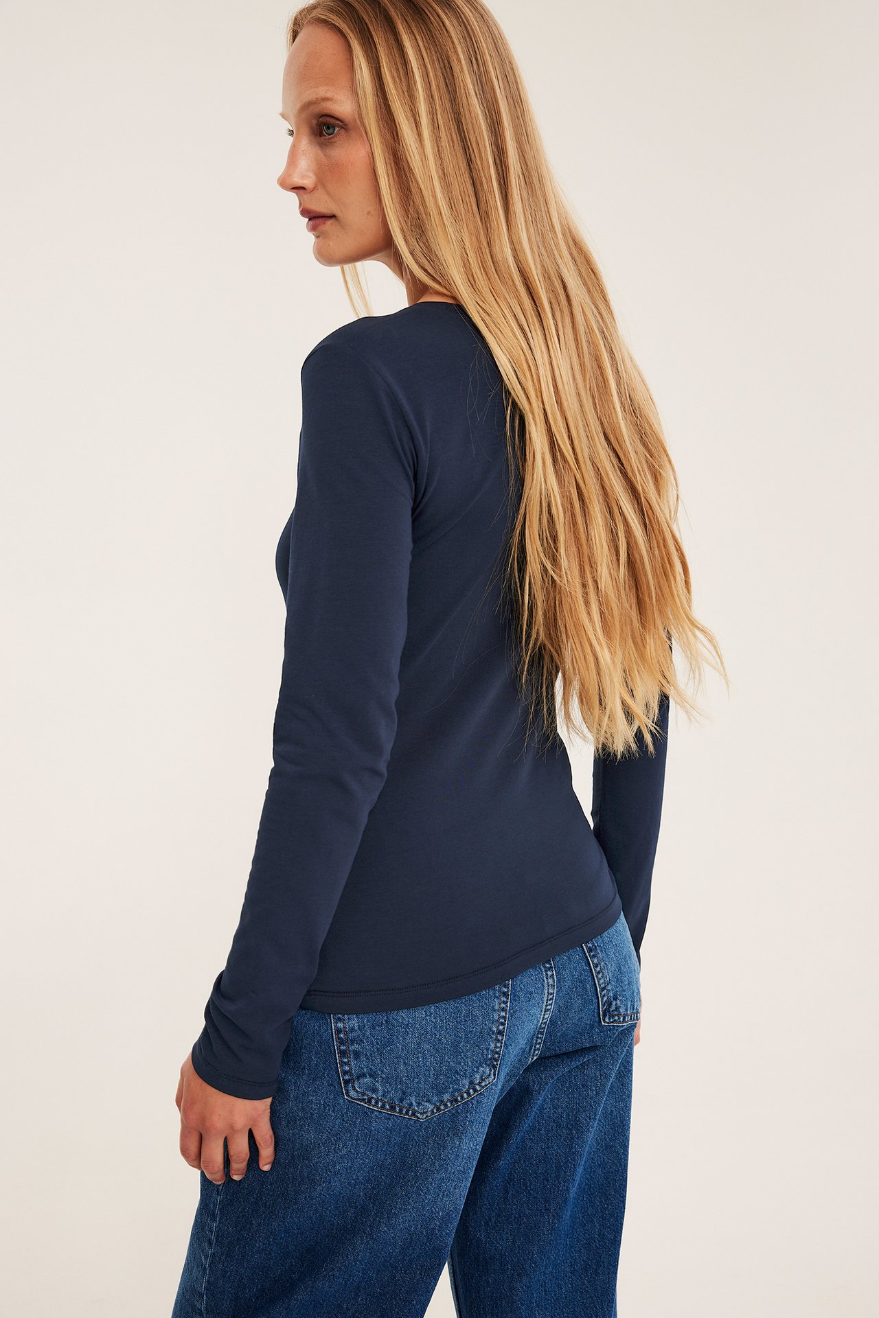 Sidovy av en kvinna som bär en mörkblå, långärmad topp med rund hals och blå jeans.