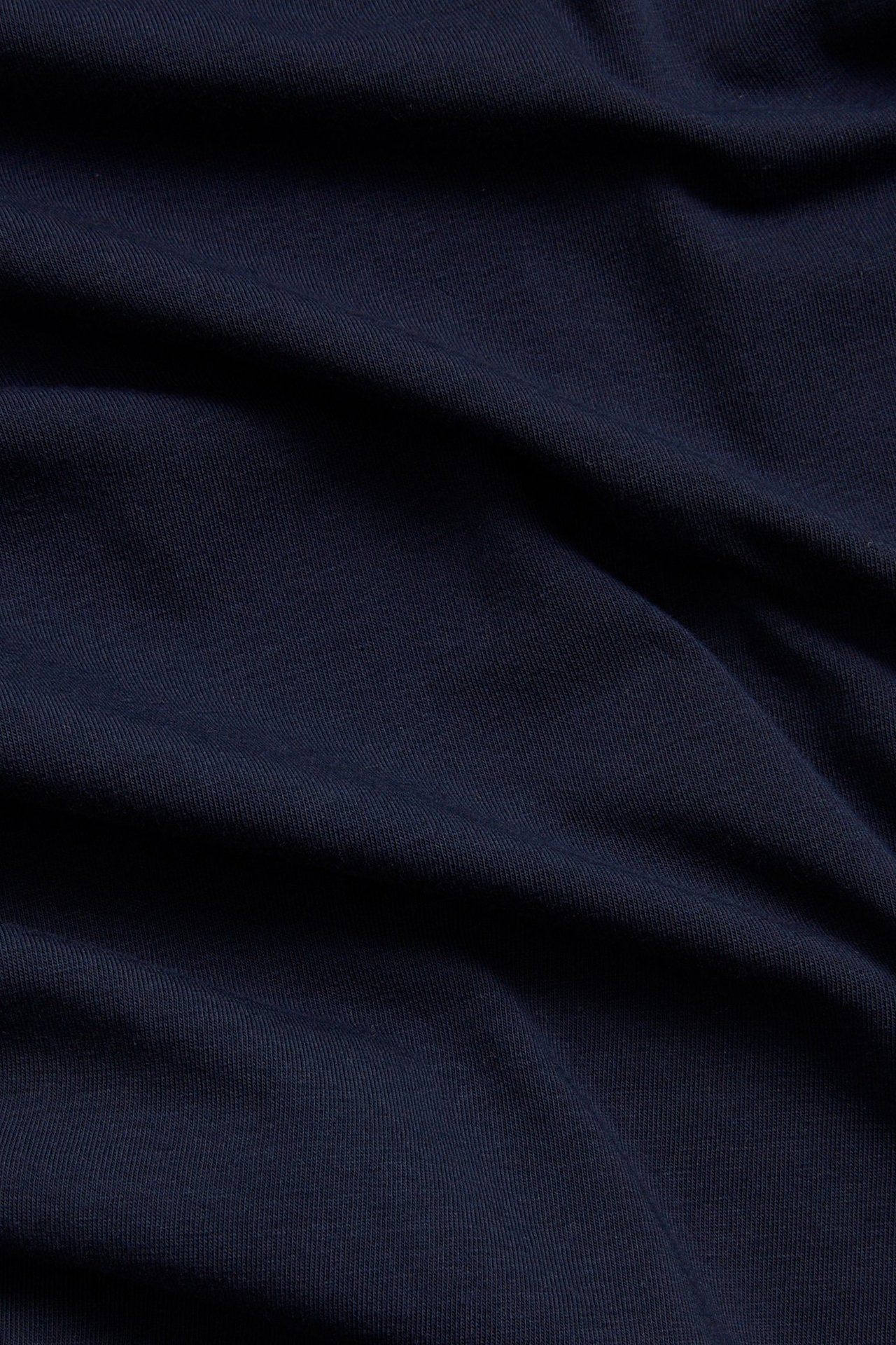 Lähikuva tummansinisestä yksivärisestä pitkähihaisesta topista joustavaa puuvillasekoitekangasta.