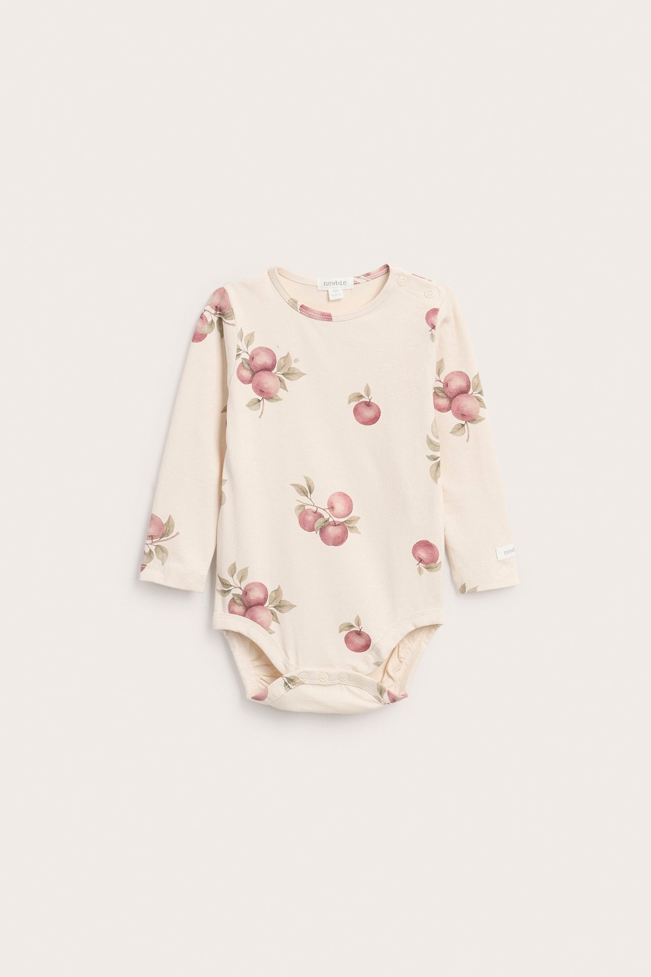 Framsida av långärmad beige babybody med rosa äppelmönster.