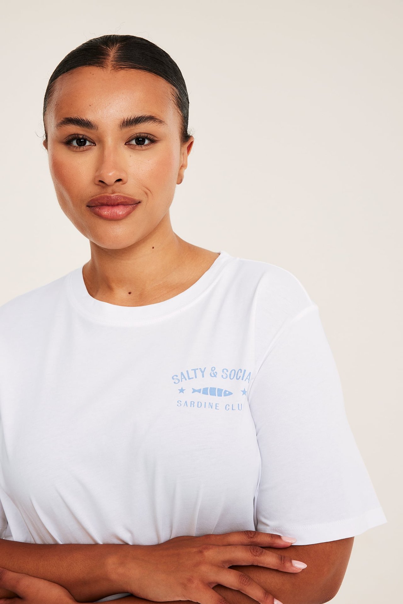 Frontbild av en kvinna i en vit kortärmad t-shirt med blått 'Salty & Social'-tryck.