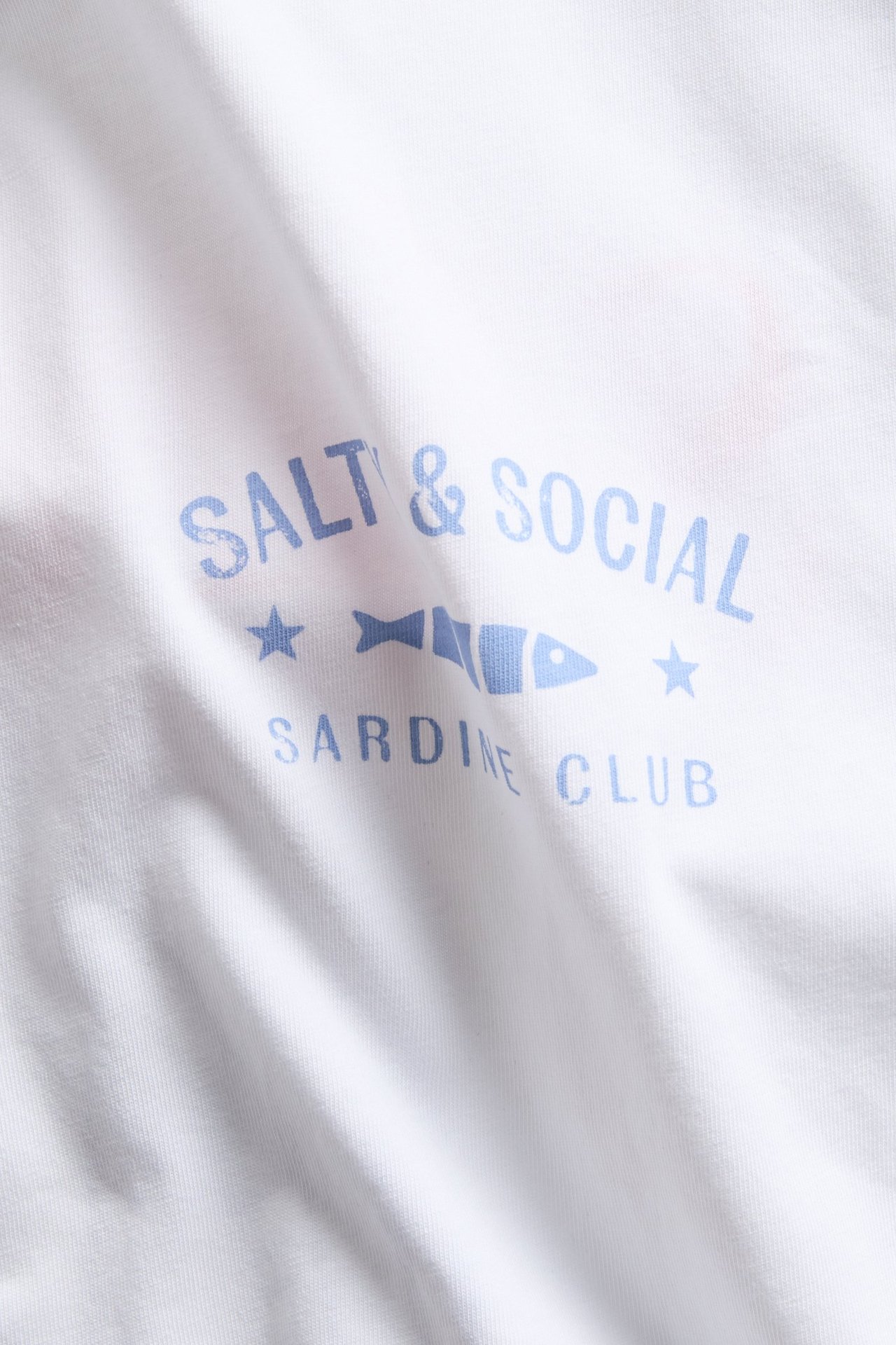 Närbild framifrån på en vit bomulls-t-shirt med blått 'Salt & Social Sardine Club' tryck.