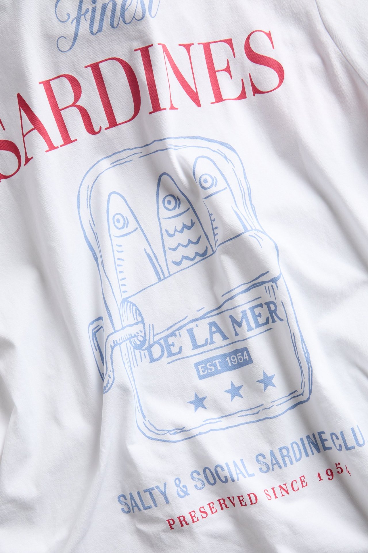Närbild av en vit bomulls-t-shirt med rött och blått sardinburksmotivtryck.