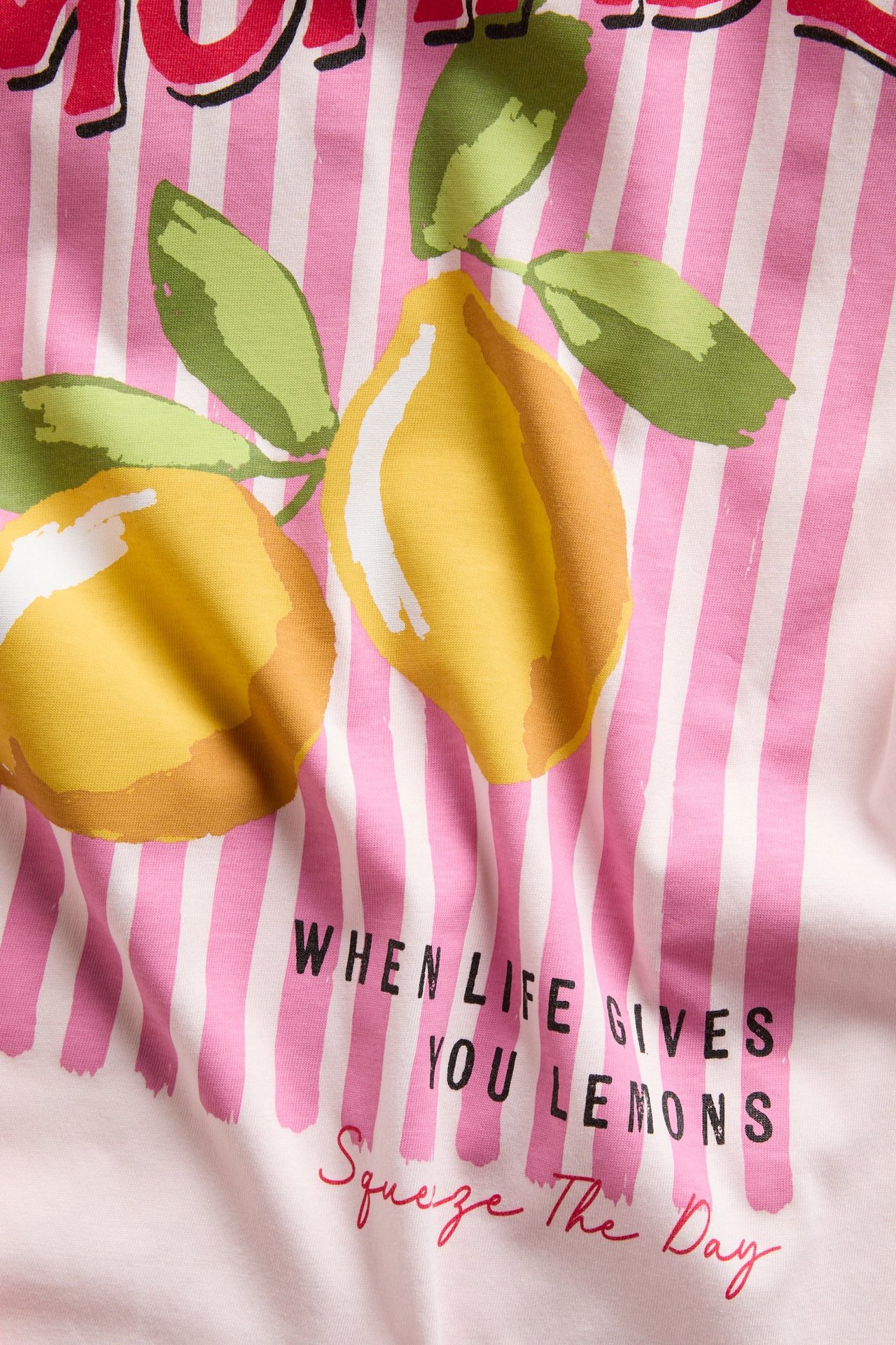Närbild på en ljusrosa bomulls-t-shirt med tryck: rosa ränder, gula citroner och citattext.