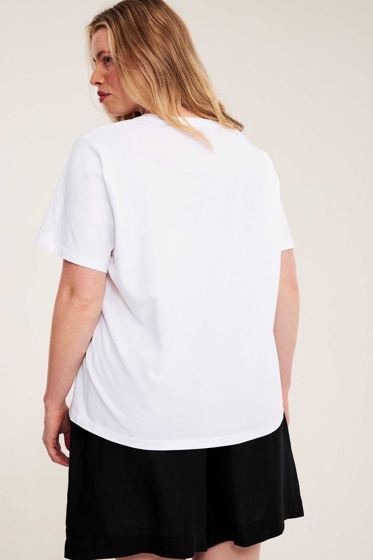 Bakifrån på en kvinna i en vit lös bomullst-shirt och svarta shorts.