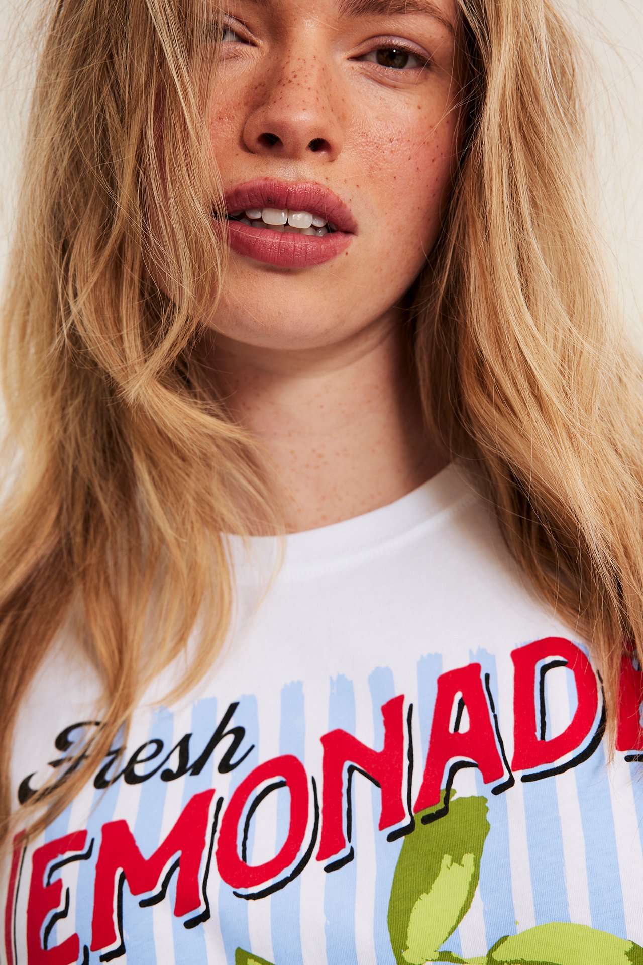 Närbild på en kvinna som bär en vit bomulls-t-shirt med tryckt "Fresh Lemonade"-motiv framtill.