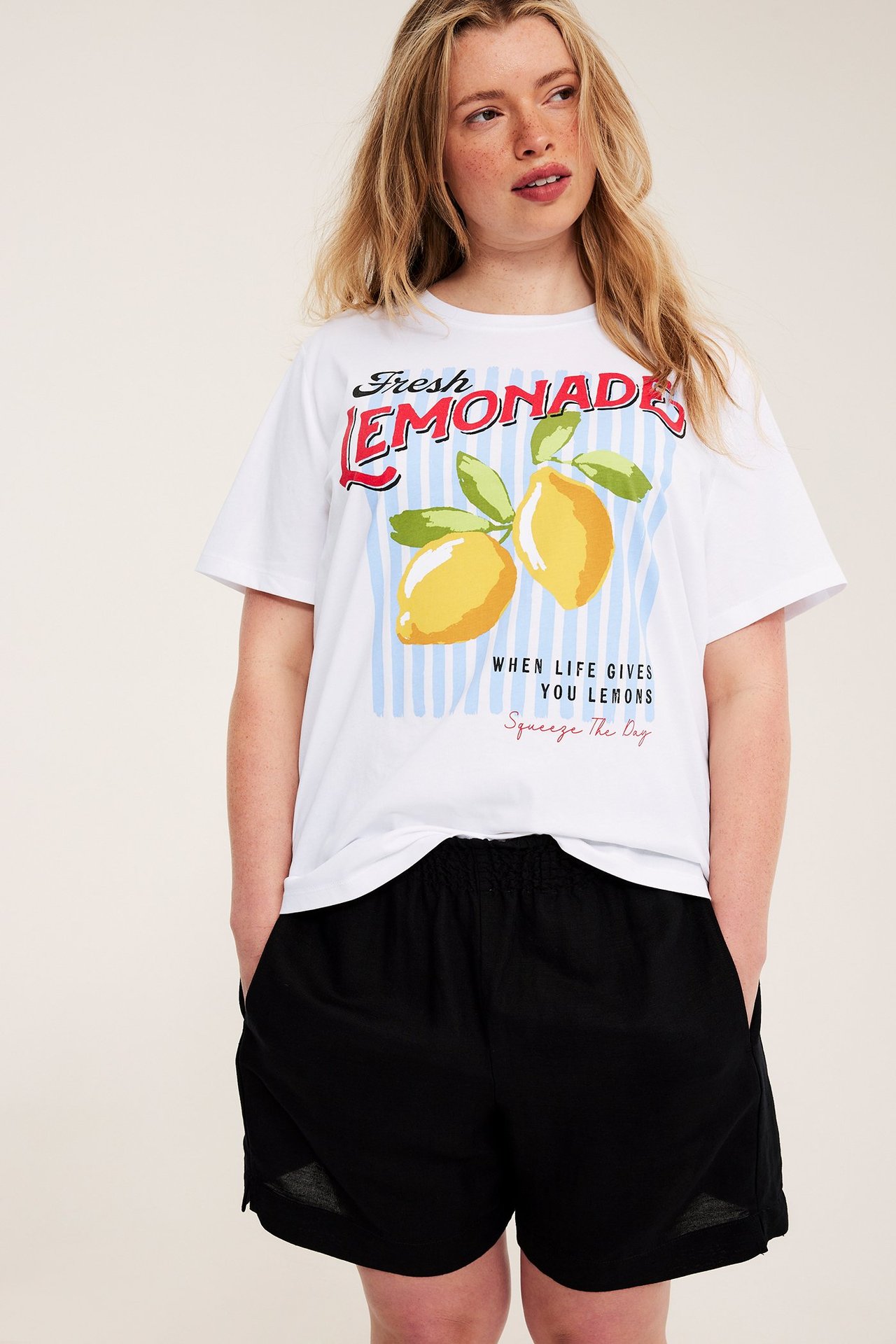 Framifrån på en kvinna i en vit t-shirt i bomull med ett "Fresh Lemonade"-tryck och svarta shorts.